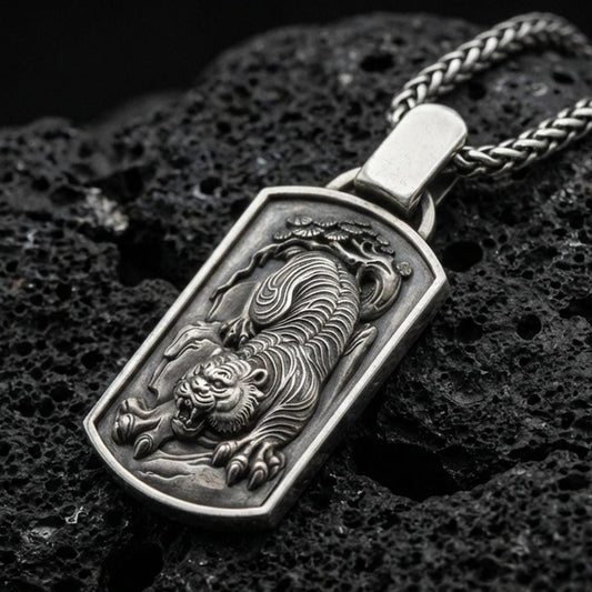 Oxidized sterling silver Chinese tiger pendant on textured volcanic rock, roaring tiger relief in rectangular tag frame, macro studio shot