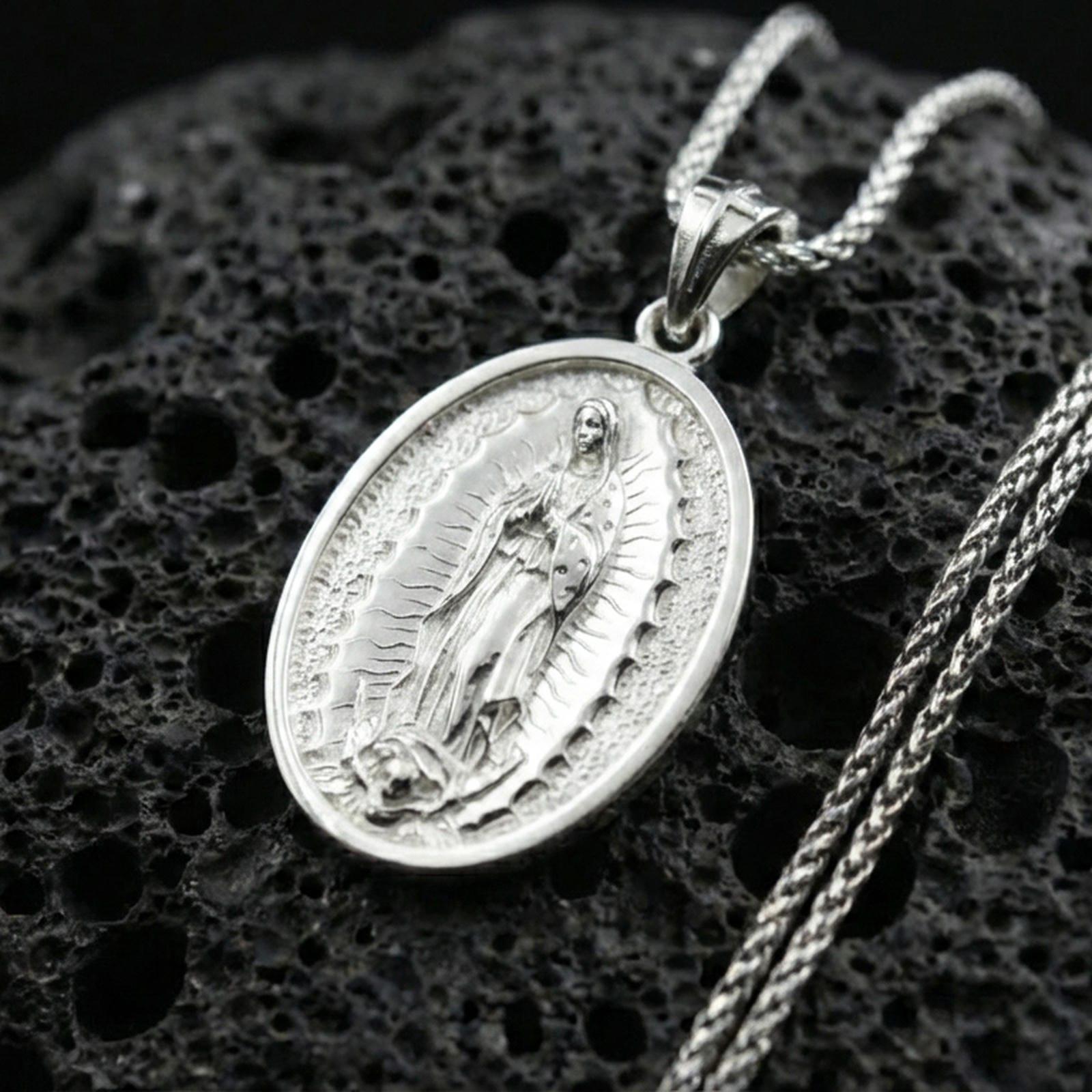Polished silver Guadalupe medallion necklace on dark volcanic stone, crisp Marian figure detail and smooth oval bezel, premium close-up composition