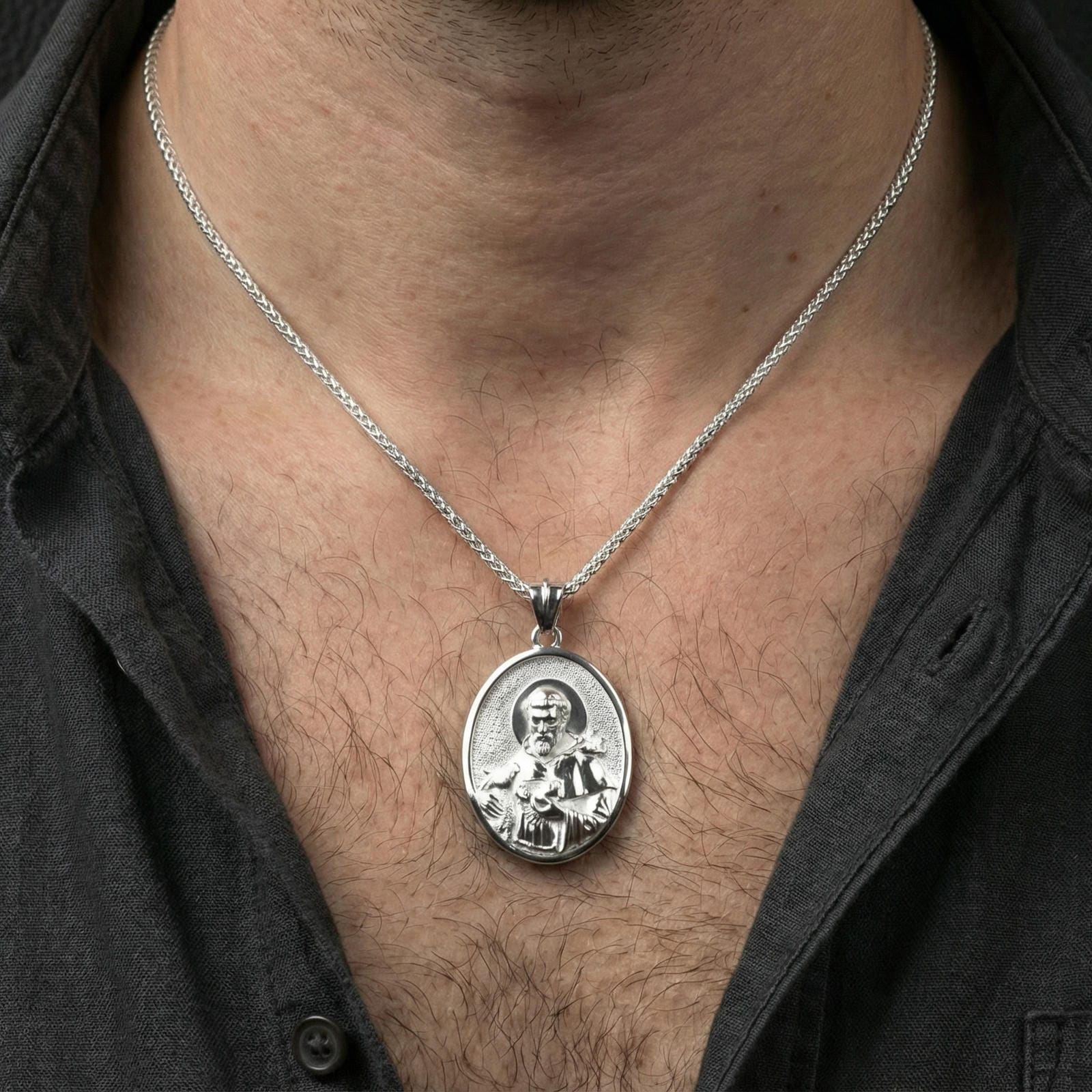 Polished silver St Francis oval pendant necklace worn on neck, close lifestyle crop, clear halo relief and portrait details