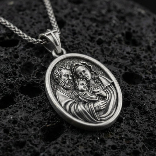 Oxidized sterling silver Holy Family oval medal on textured volcanic rock, detailed Mary Joseph and Child relief, macro studio shot