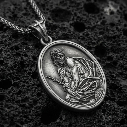 Oxidized sterling silver Jesus Christ oval medal on textured volcanic rock, detailed religious relief with crown of thorns, macro studio shot