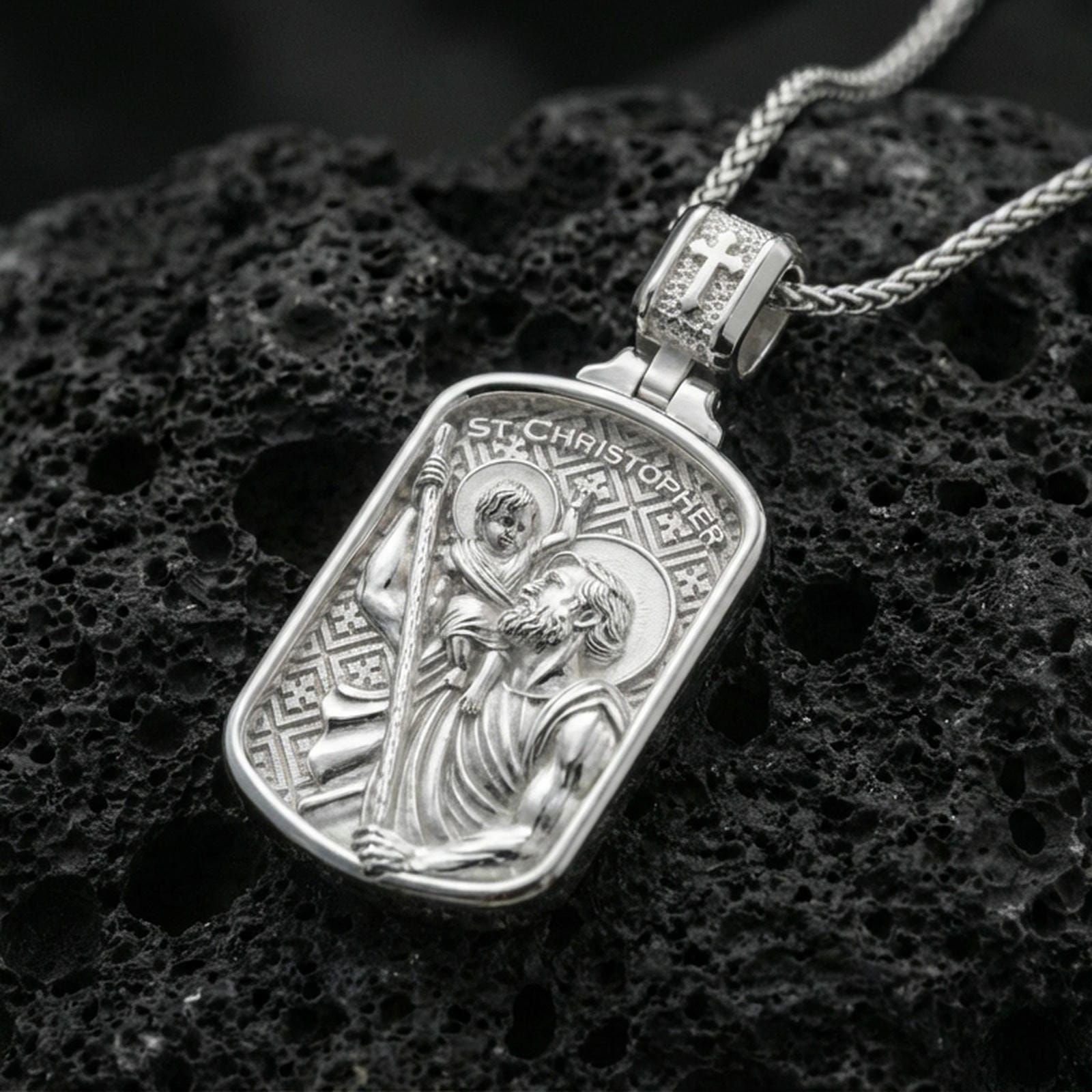 Polished silver St Christopher necklace pendant on dark volcanic stone, crisp “St Christopher” text and detailed figure engraving, premium close-up