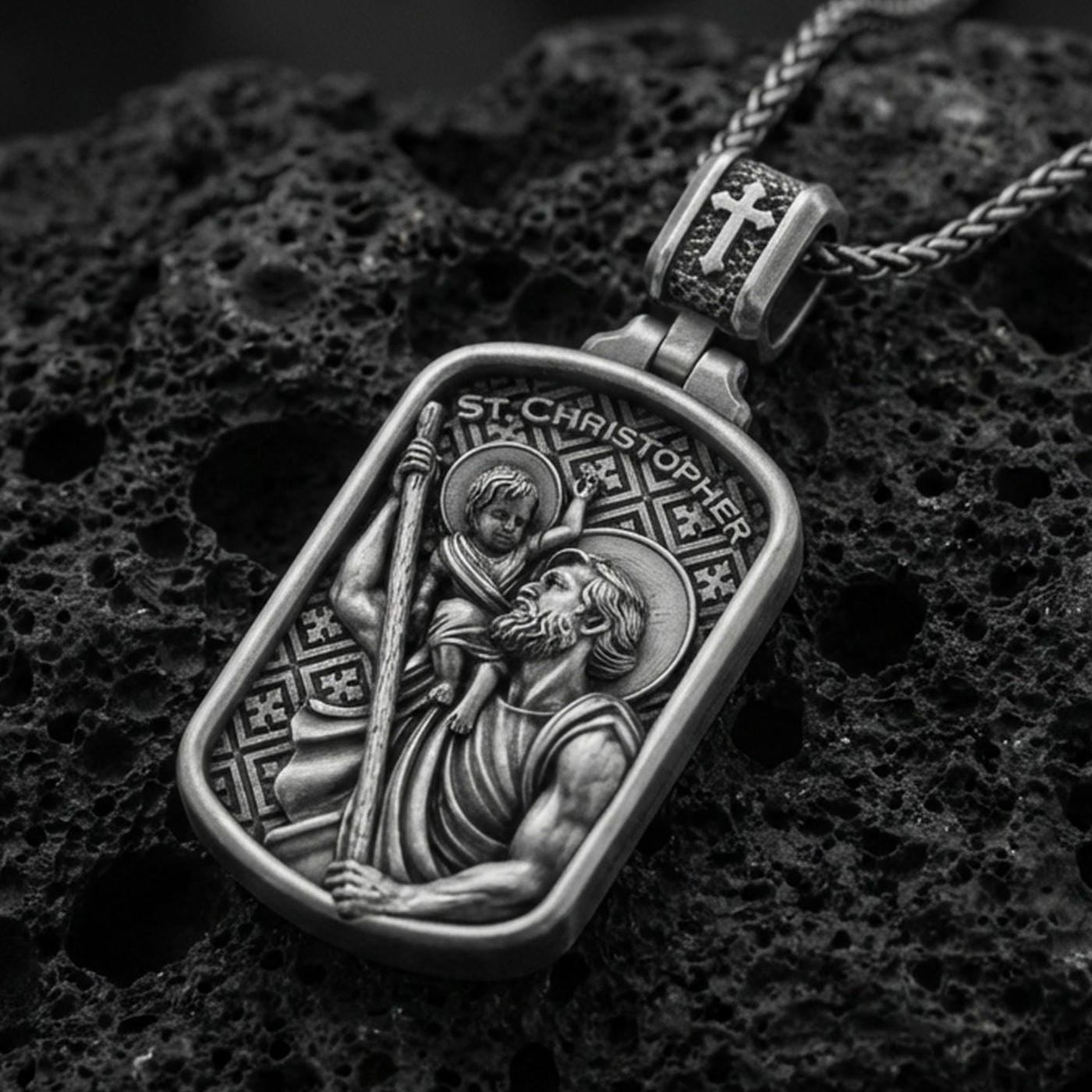 Oxidized sterling silver Saint Christopher pendant on textured volcanic rock, rectangular medal with saint carrying child relief, macro studio shot