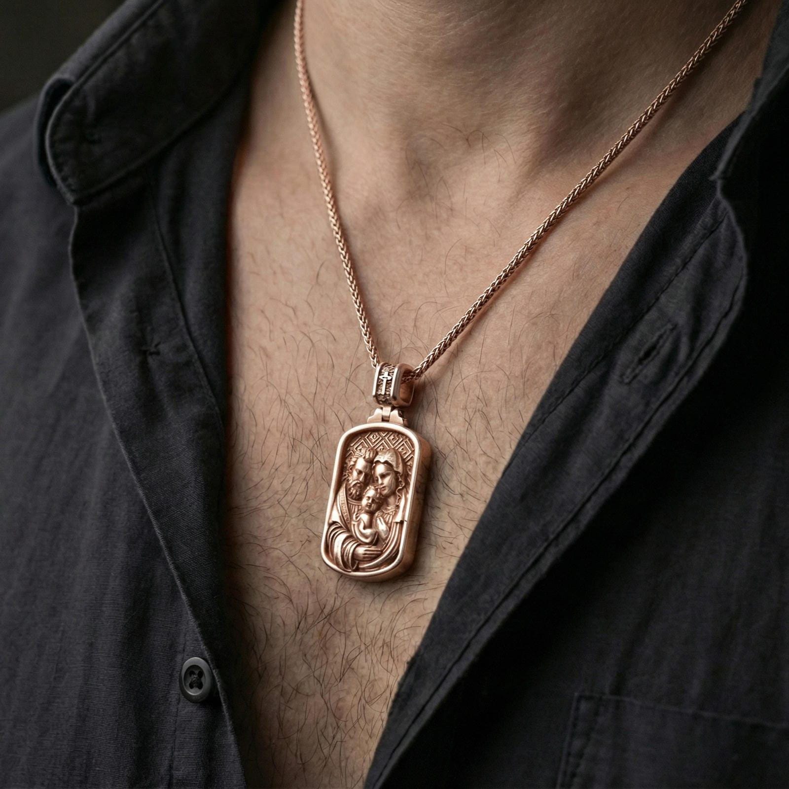 Rose gold plated Holy Family pendant worn on neck, detailed Mary Joseph and Child relief, clean lifestyle framing with dark shirt contrast