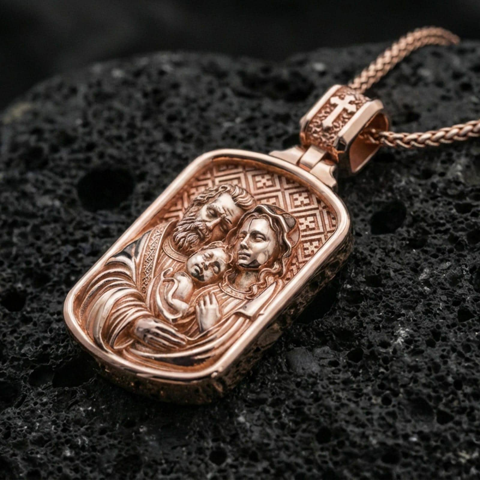 Rose gold plated Holy Family medallion pendant on matte volcanic stone, intricate religious engraving and framed rectangular edge, sharp macro focus