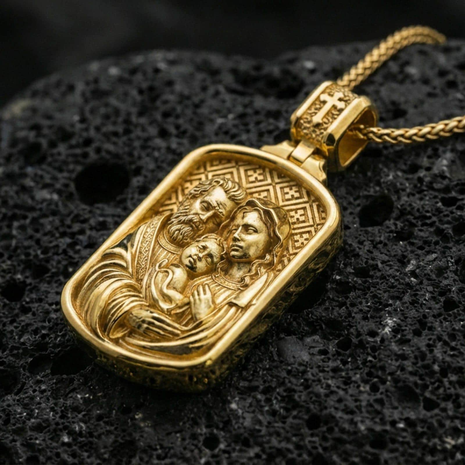Gold plated Holy Family pendant on porous volcanic rock backdrop, rectangular devotional medal with detailed family relief, high-contrast lighting