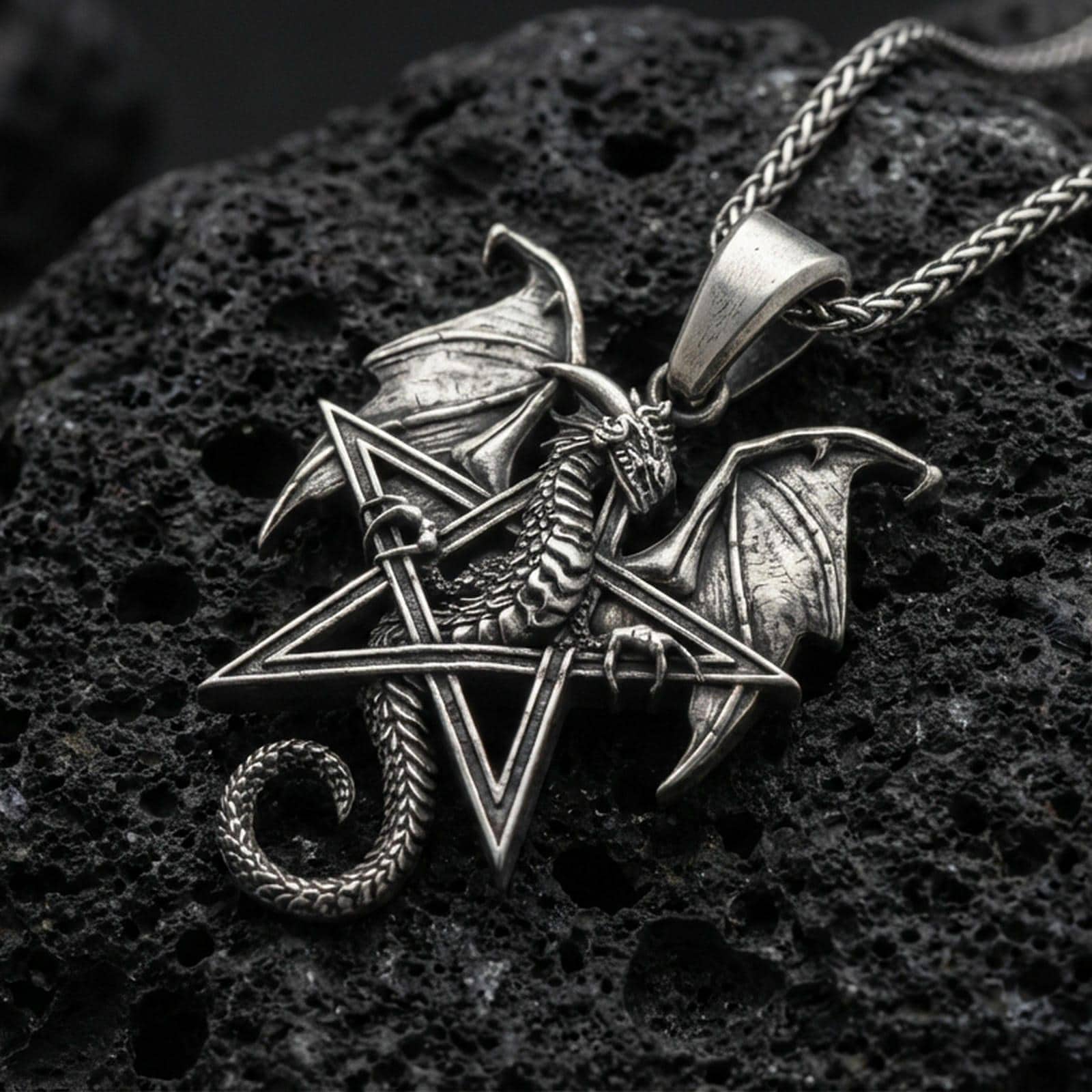 Oxidized sterling silver pentagram dragon pendant on textured volcanic rock, winged dragon wrapped around star frame, macro studio shot