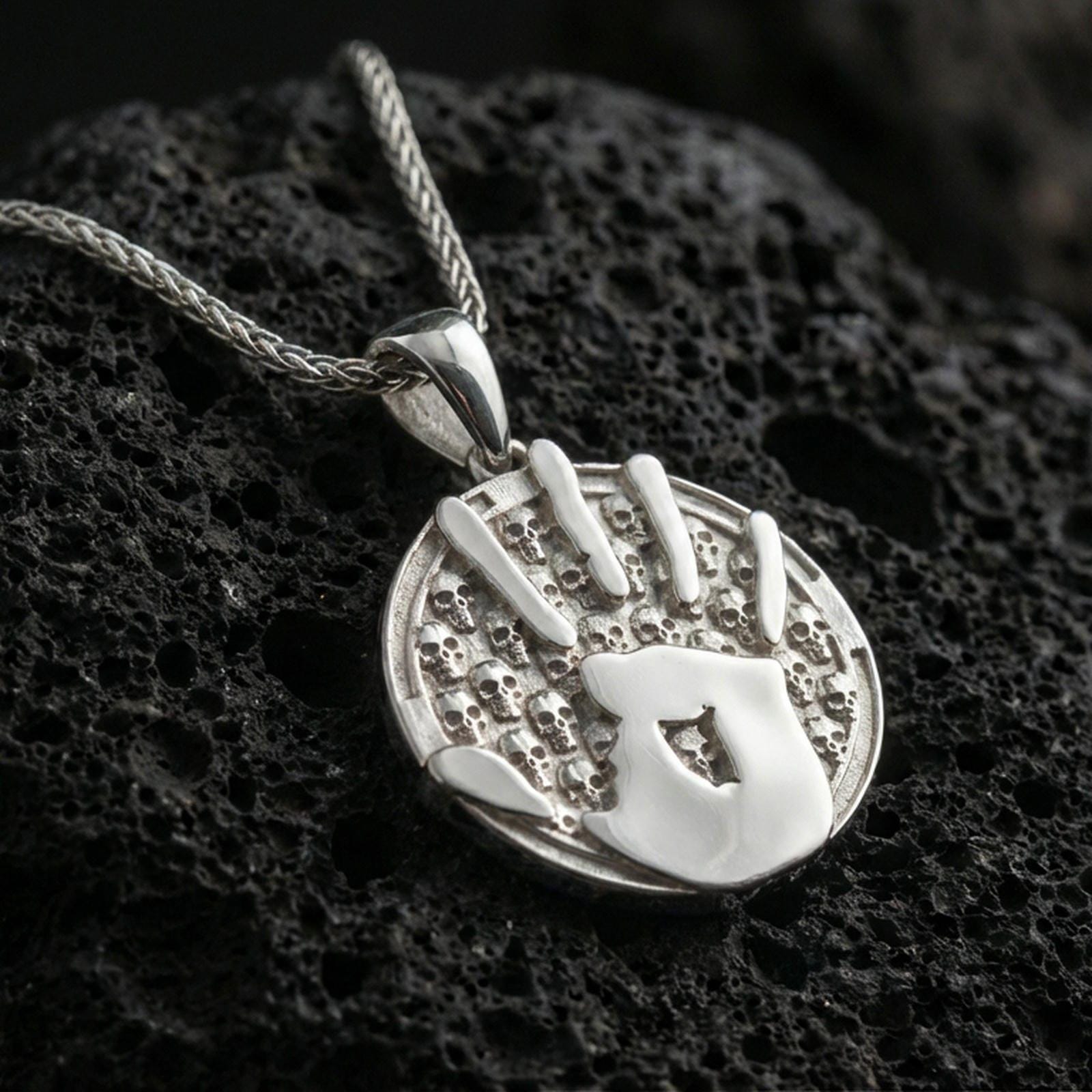 Polished silver Dark Brotherhood handprint pendant necklace on dark volcanic stone, crisp raised emblem and detailed skull texture, premium close-up