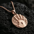 Load image into Gallery viewer, Rose gold plated Dark Brotherhood handprint pendant on matte volcanic stone, detailed skull motif background with bold emblem centerpiece, sharp macro focus
