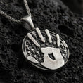 Load image into Gallery viewer, Oxidized sterling silver Skyrim Dark Brotherhood pendant on textured volcanic rock, iconic handprint emblem over skull pattern background, macro studio shot
