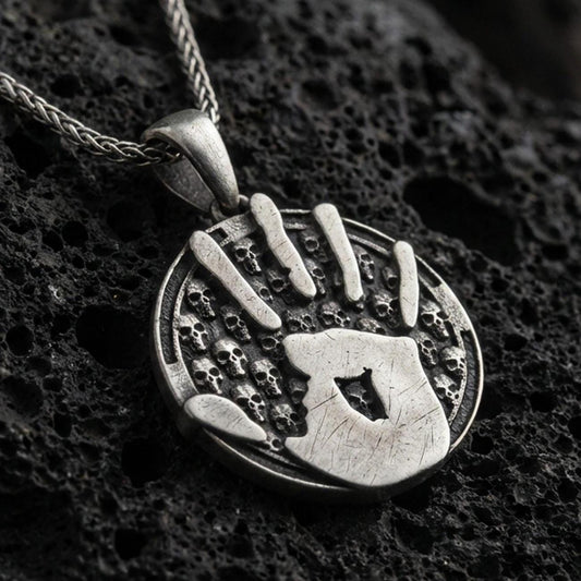 Oxidized sterling silver Skyrim Dark Brotherhood pendant on textured volcanic rock, iconic handprint emblem over skull pattern background, macro studio shot