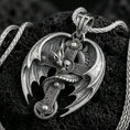 Load image into Gallery viewer, Oxidized sterling silver dragon cross pendant on textured volcanic rock, gothic winged dragon wrapped around medieval cross with skull detail, macro studio shot
