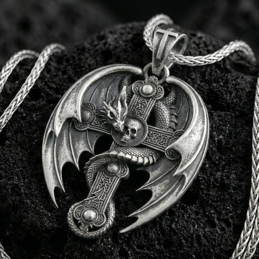 Oxidized sterling silver dragon cross pendant on textured volcanic rock, gothic winged dragon wrapped around medieval cross with skull detail, macro studio shot
