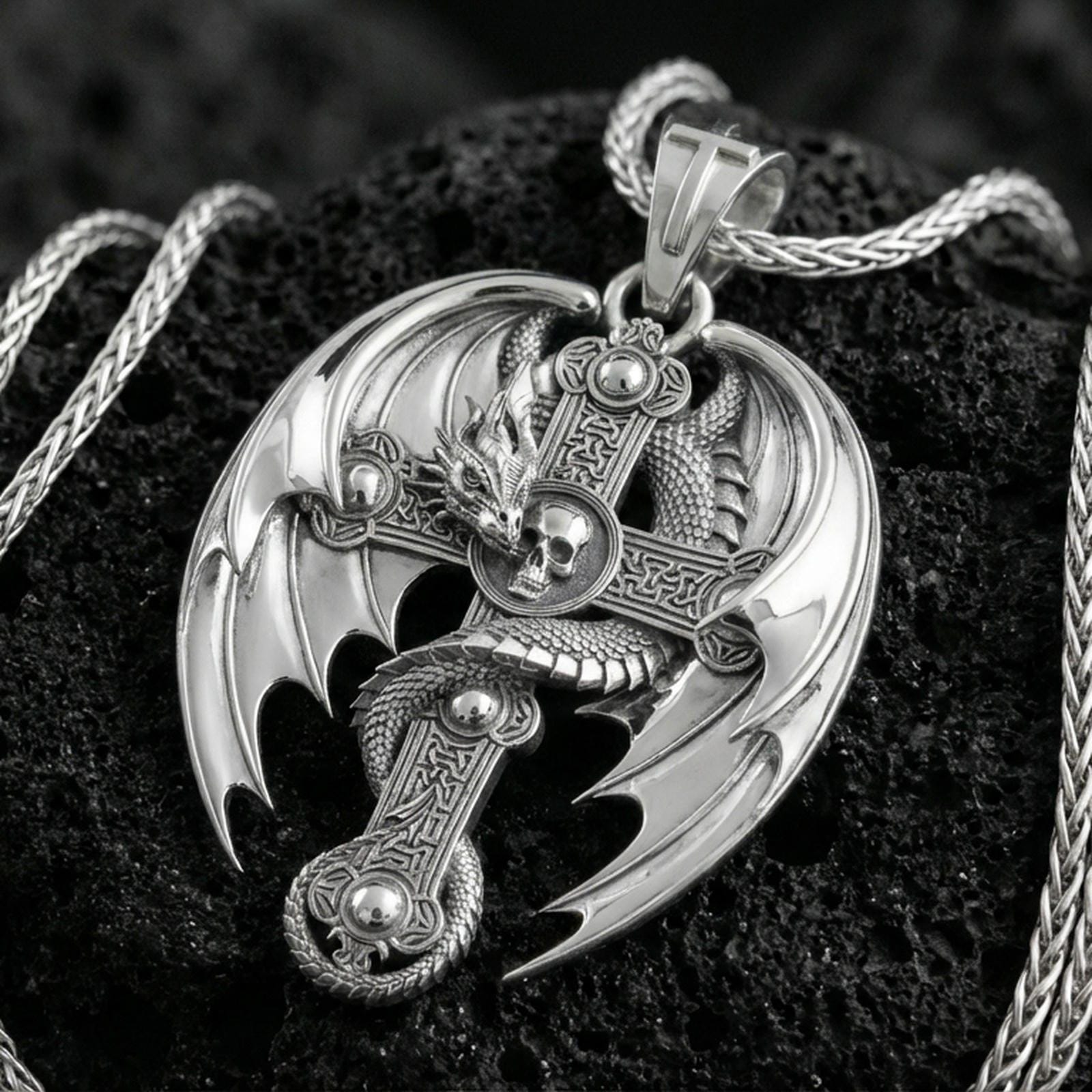 Polished silver dragon cross necklace pendant on dark volcanic stone, crisp wing edges and engraved cross pattern, premium close-up composition