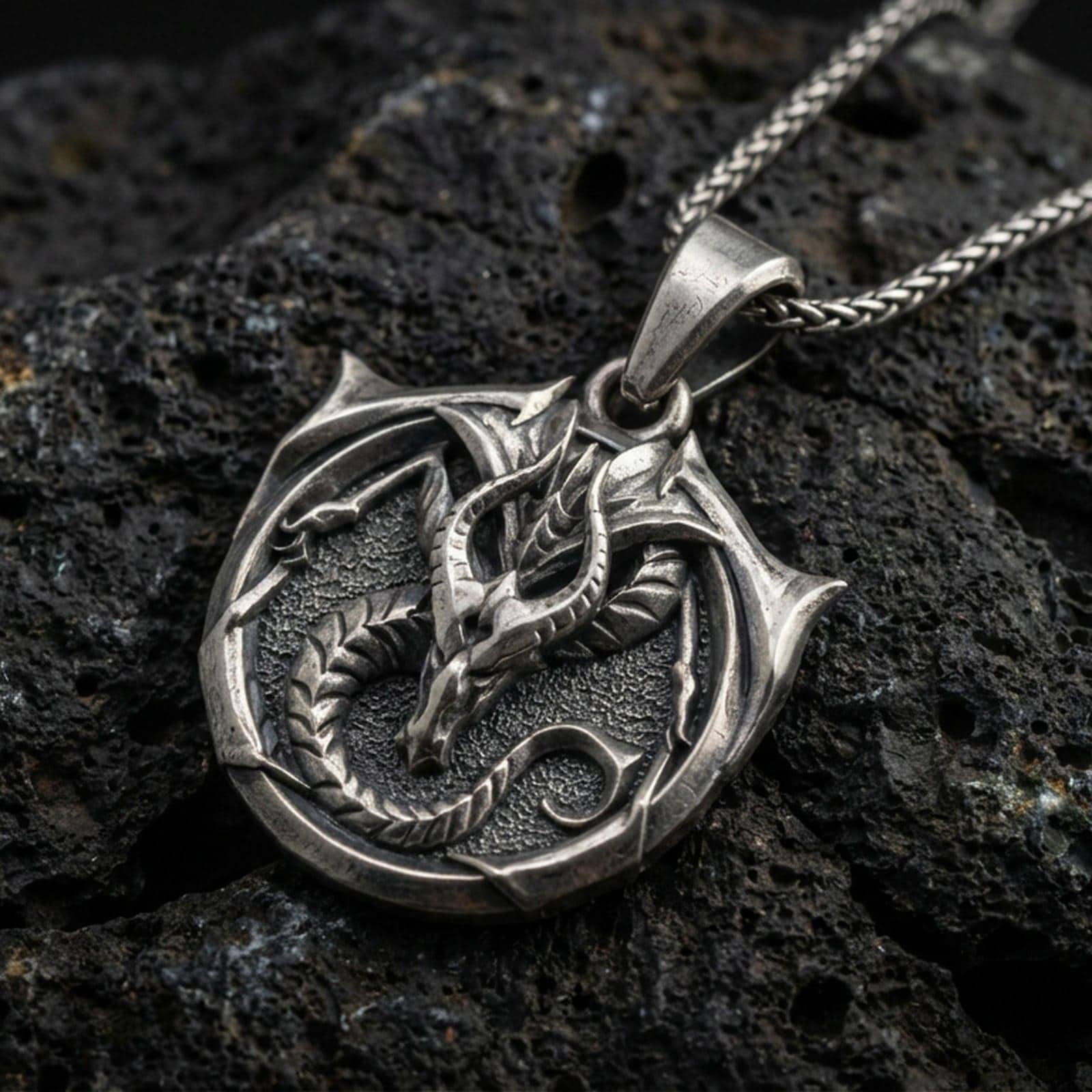Oxidized sterling silver dragon pendant on volcanic rock, coiled mythical warrior amulet necklace closeup