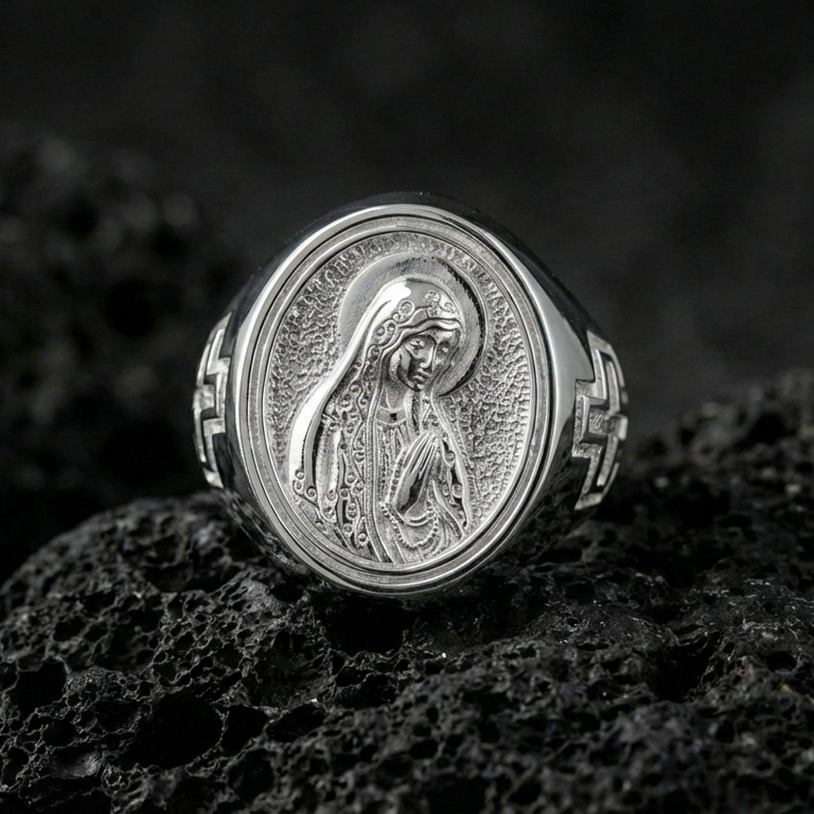 Polished silver Our Lady of Guadalupe oval signet ring on porous volcanic stone, reflective Catholic ring, studio detail
