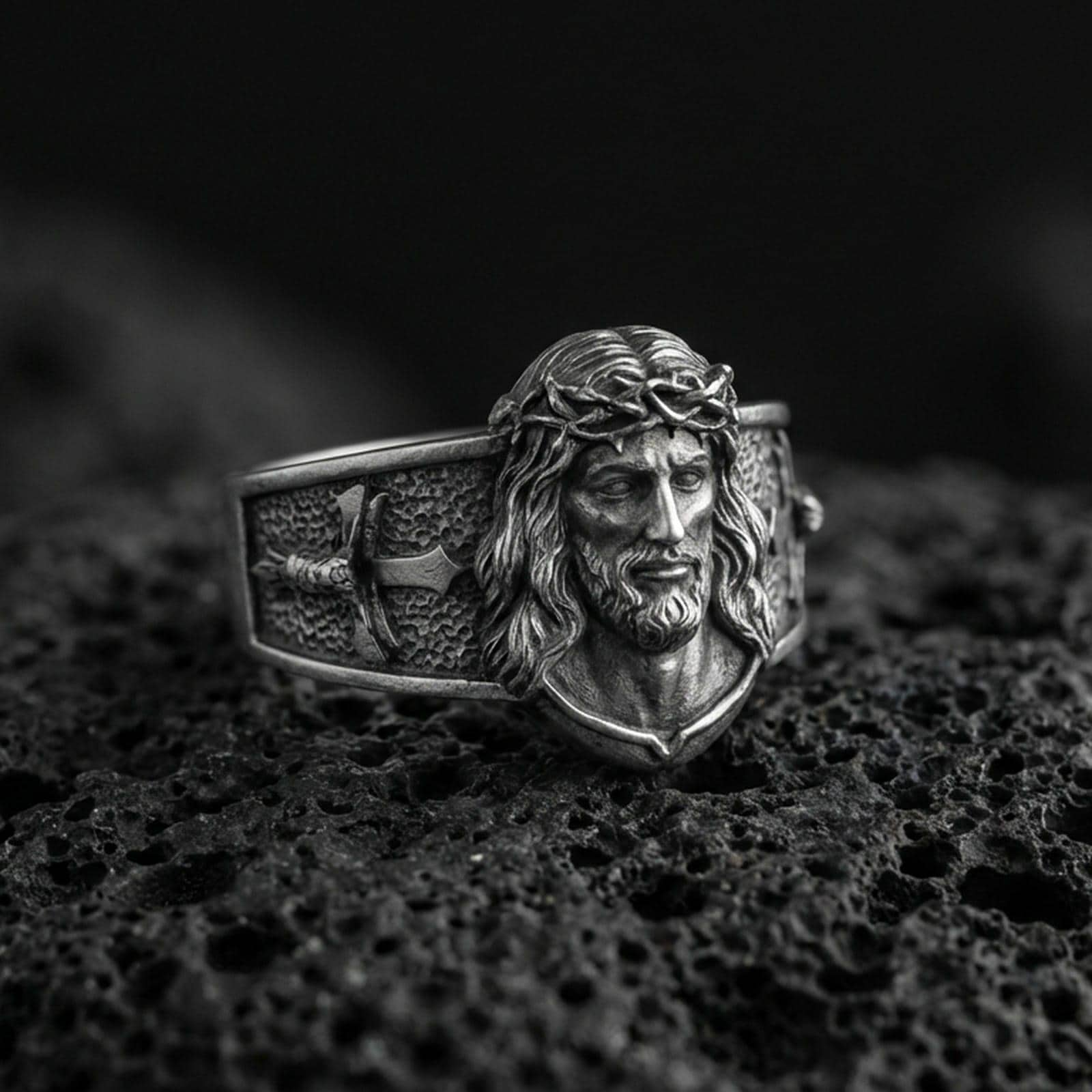 Oxidized sterling silver Jesus Christ ring on volcanic rock, crowned Christ face relief, cross motif band, macro photo