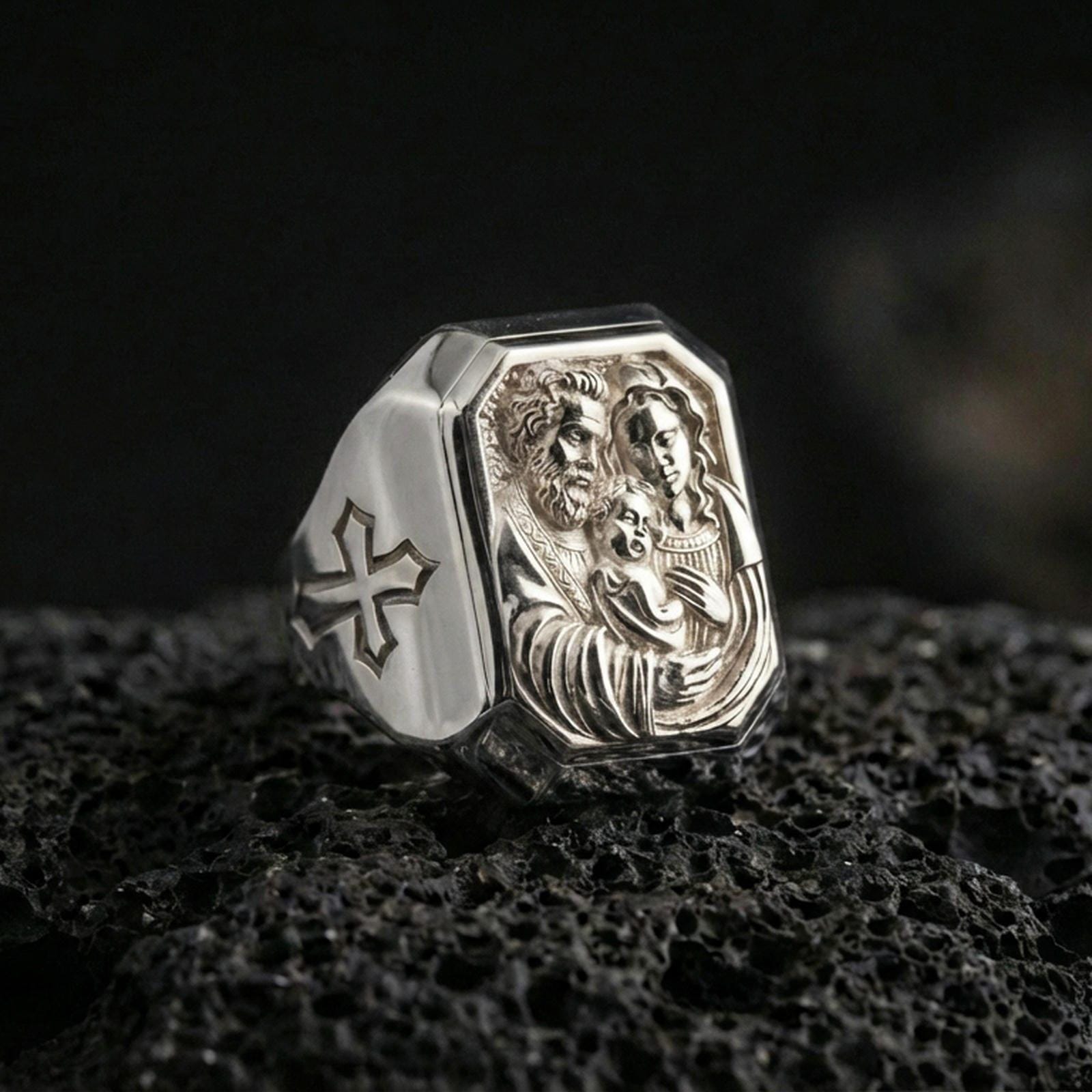 Polished silver Holy Family signet ring on porous volcanic stone, detailed family portrait engraving, Catholic jewelry macro