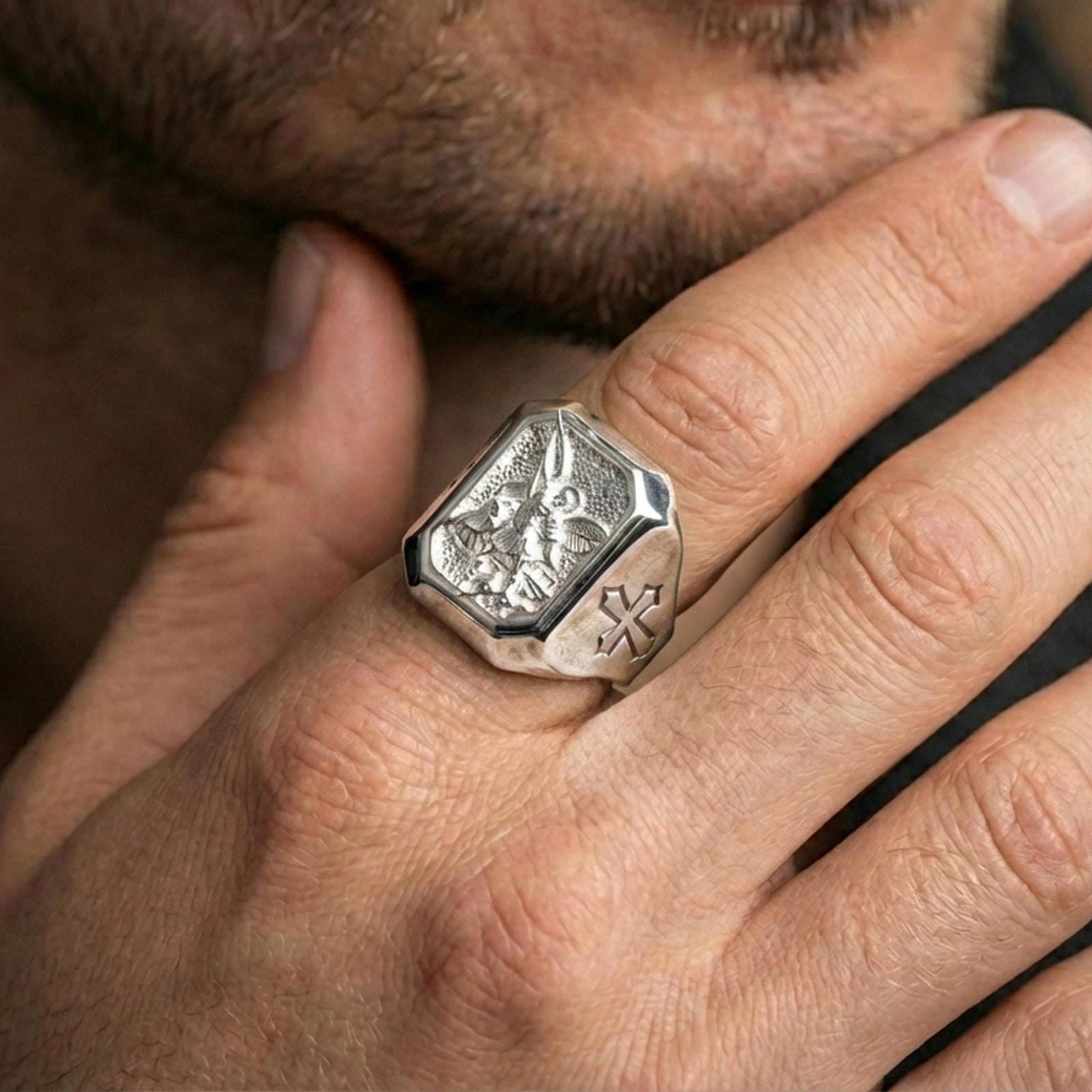 Polished silver Saint Michael signet ring worn on finger, angel protector relief, Catholic warrior ring close-up