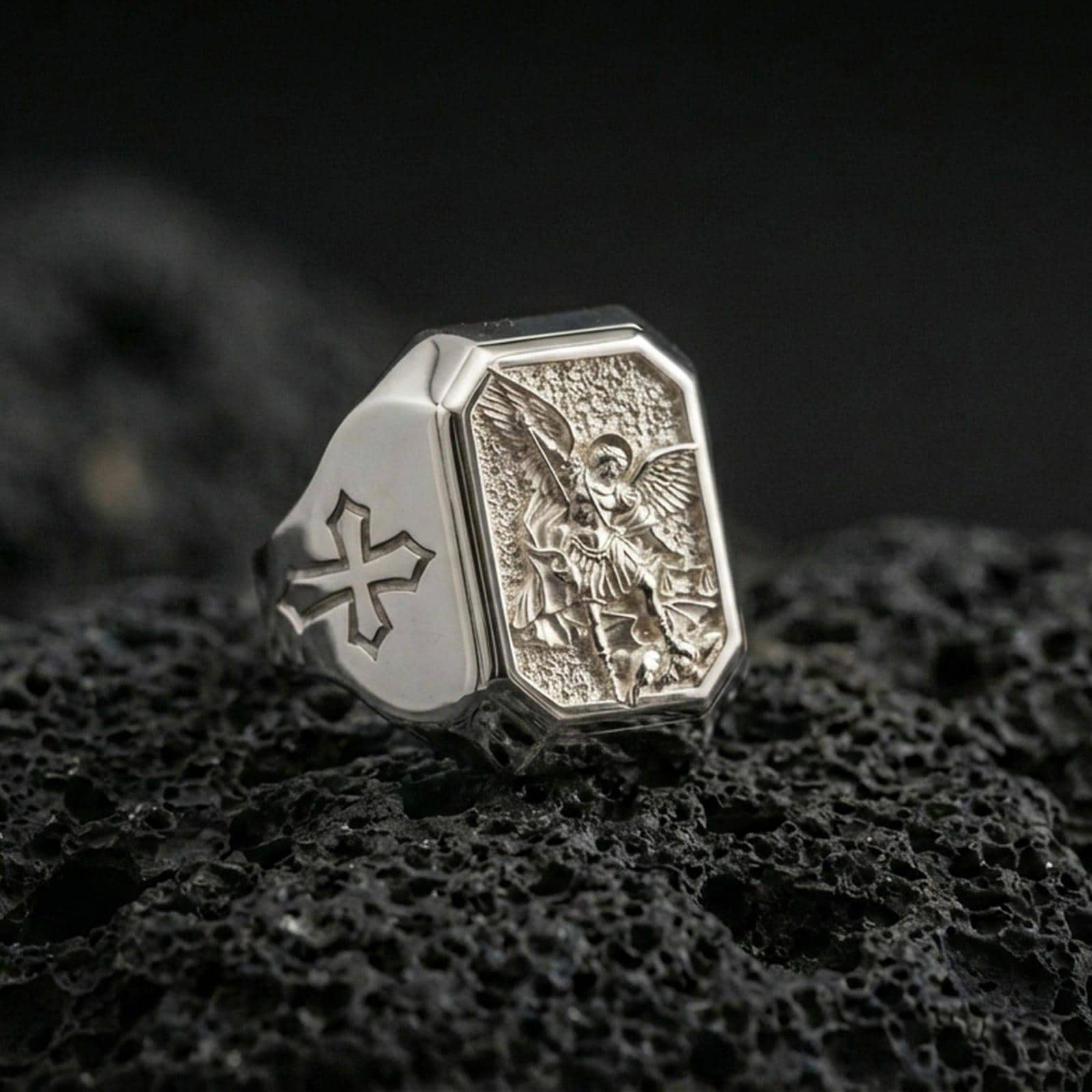Polished silver Saint Michael ring on porous volcanic stone, angel defeating dragon engraving, Templar cross detail