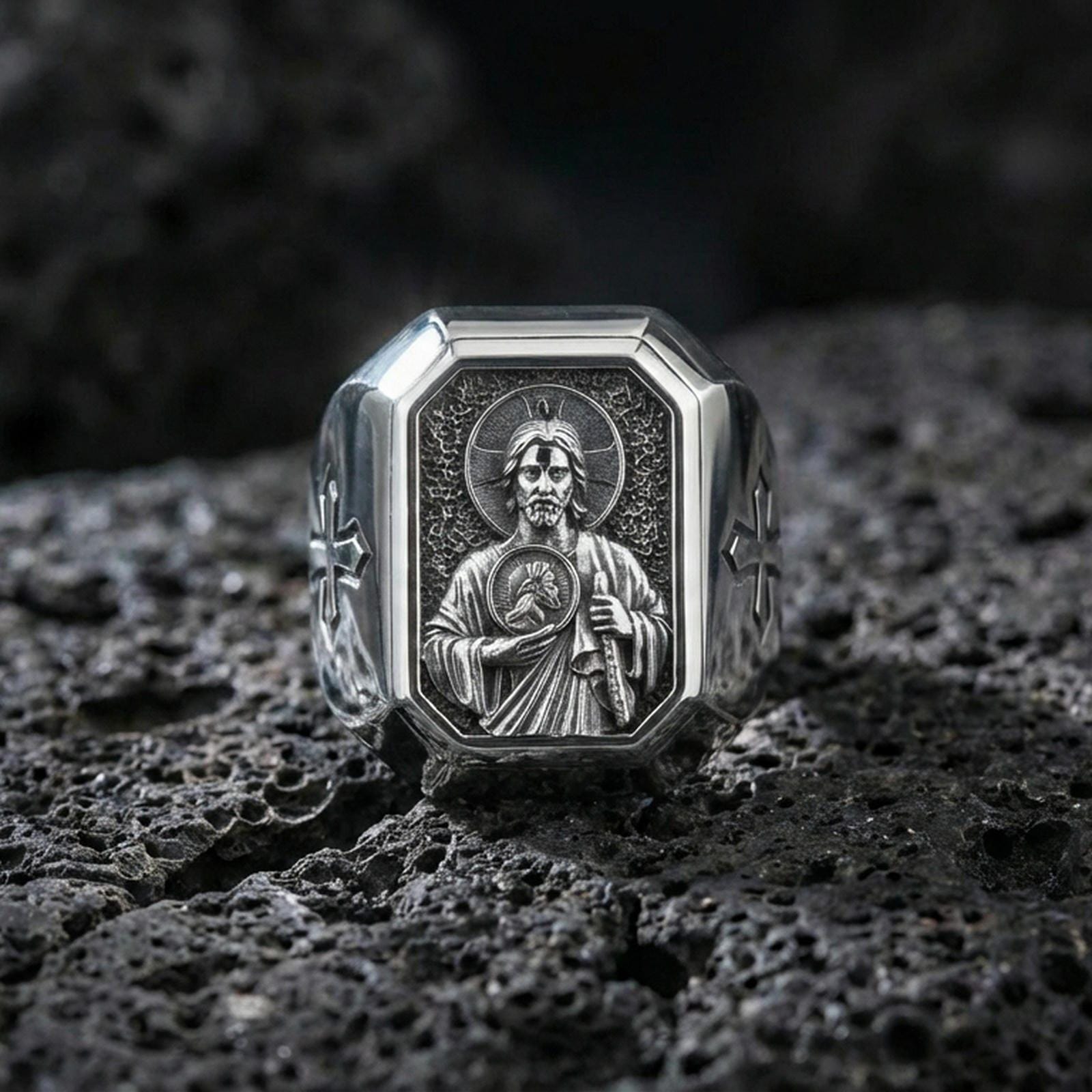 Polished silver St Jude ring on porous volcanic stone, detailed halo relief, Christian signet style