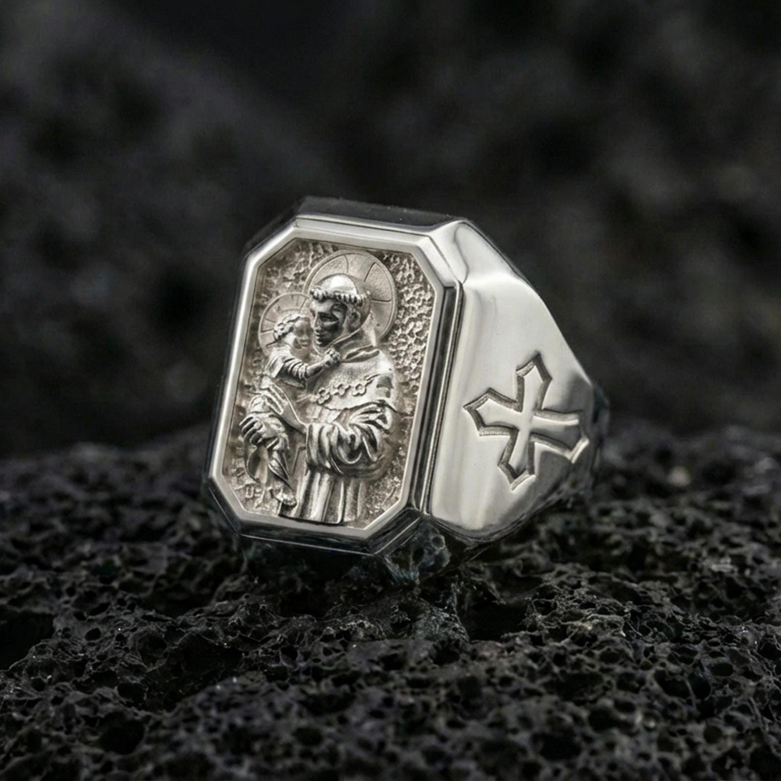 Polished silver St Anthony ring on porous volcanic stone, detailed saint portrait carving, Christian signet jewelry