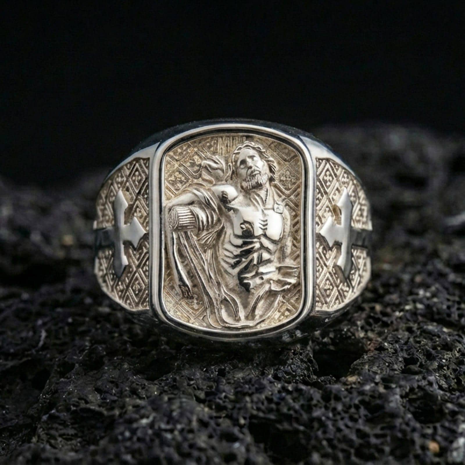 Polished silver St Sebastian signet ring on porous volcanic stone, detailed saint engraving, Christian cross shoulders close-up