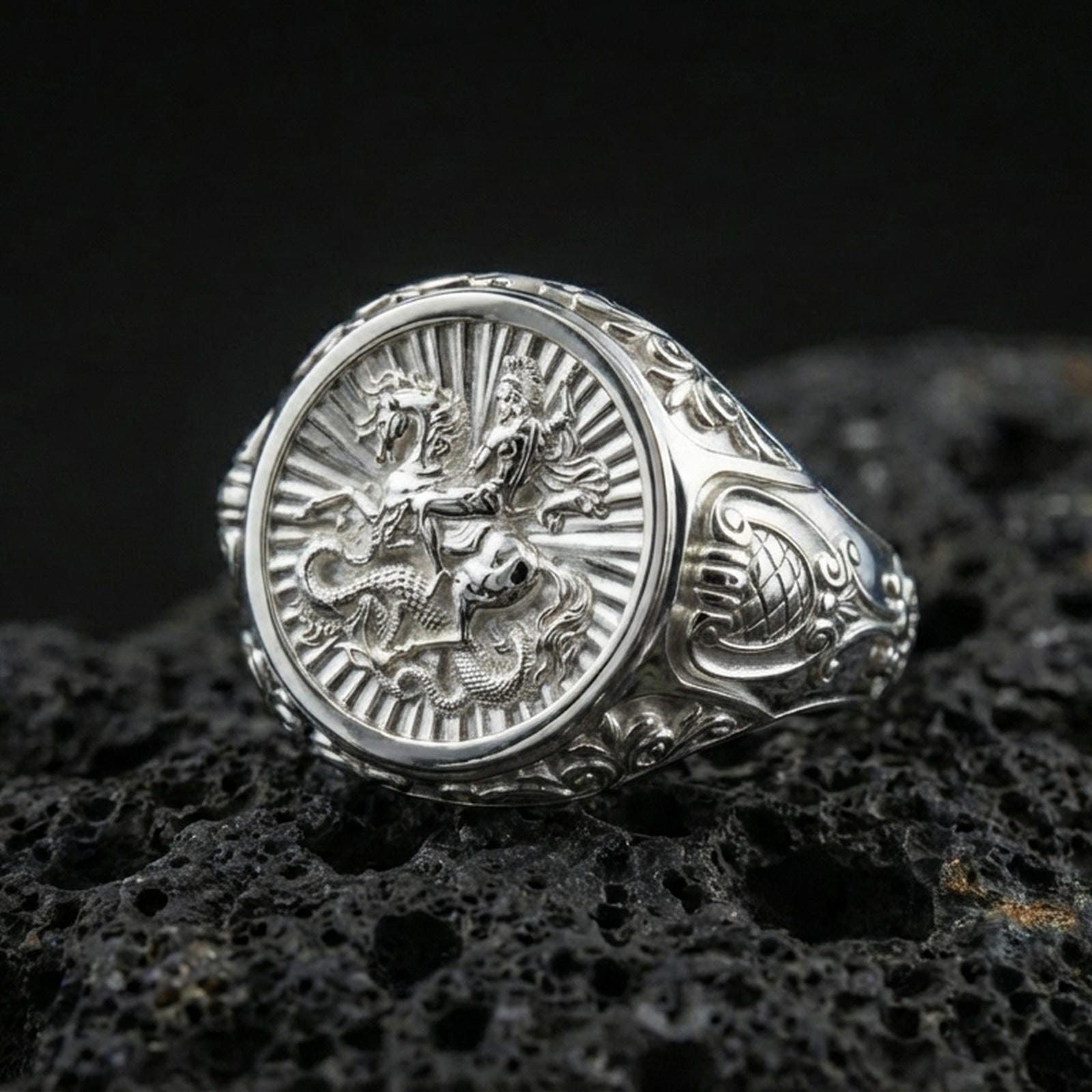 Polished silver St George ring on porous volcanic stone, detailed dragon battle engraving, religious warrior signet ring