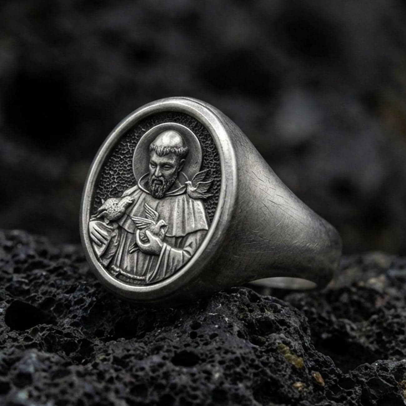 Oxidized sterling silver St Francis signet ring on volcanic rock, detailed saint relief portrait