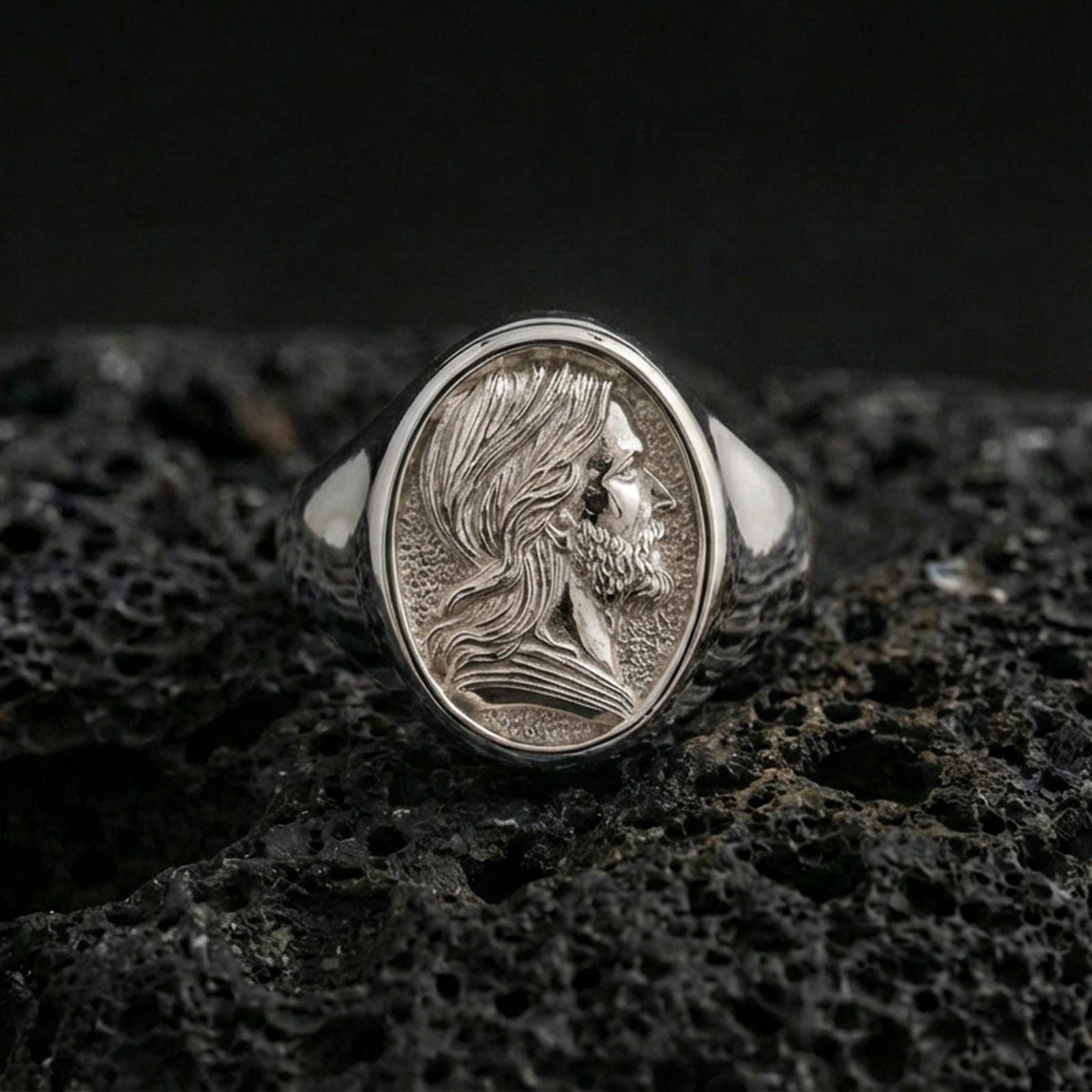 Polished silver Jesus portrait ring on volcanic stone, Christian signet jewelry closeup