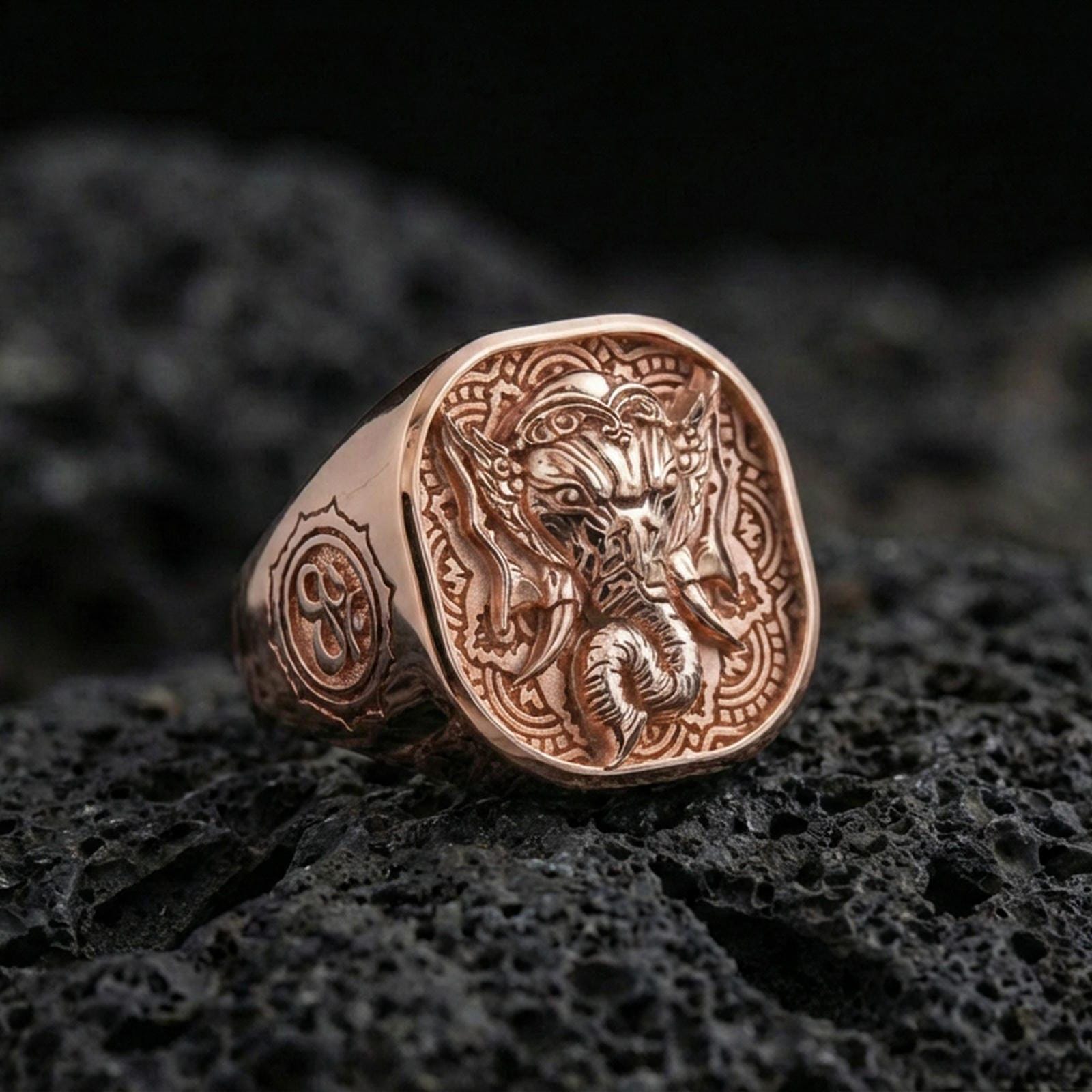 Rose gold plated Lord Ganesha ring on volcanic stone, ornate Indian pattern background, sacred symbol accessory