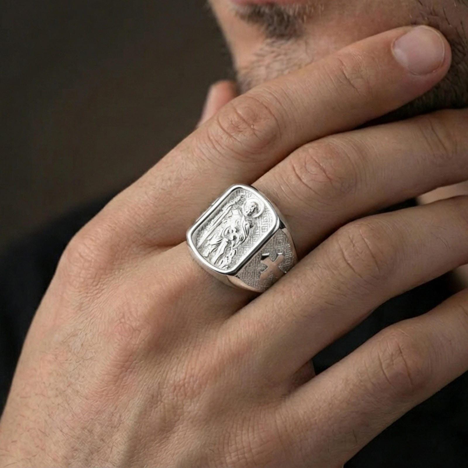 Polished silver Saint Roch signet ring worn on finger, religious protection symbol, detailed saint relief and patterned shoulders