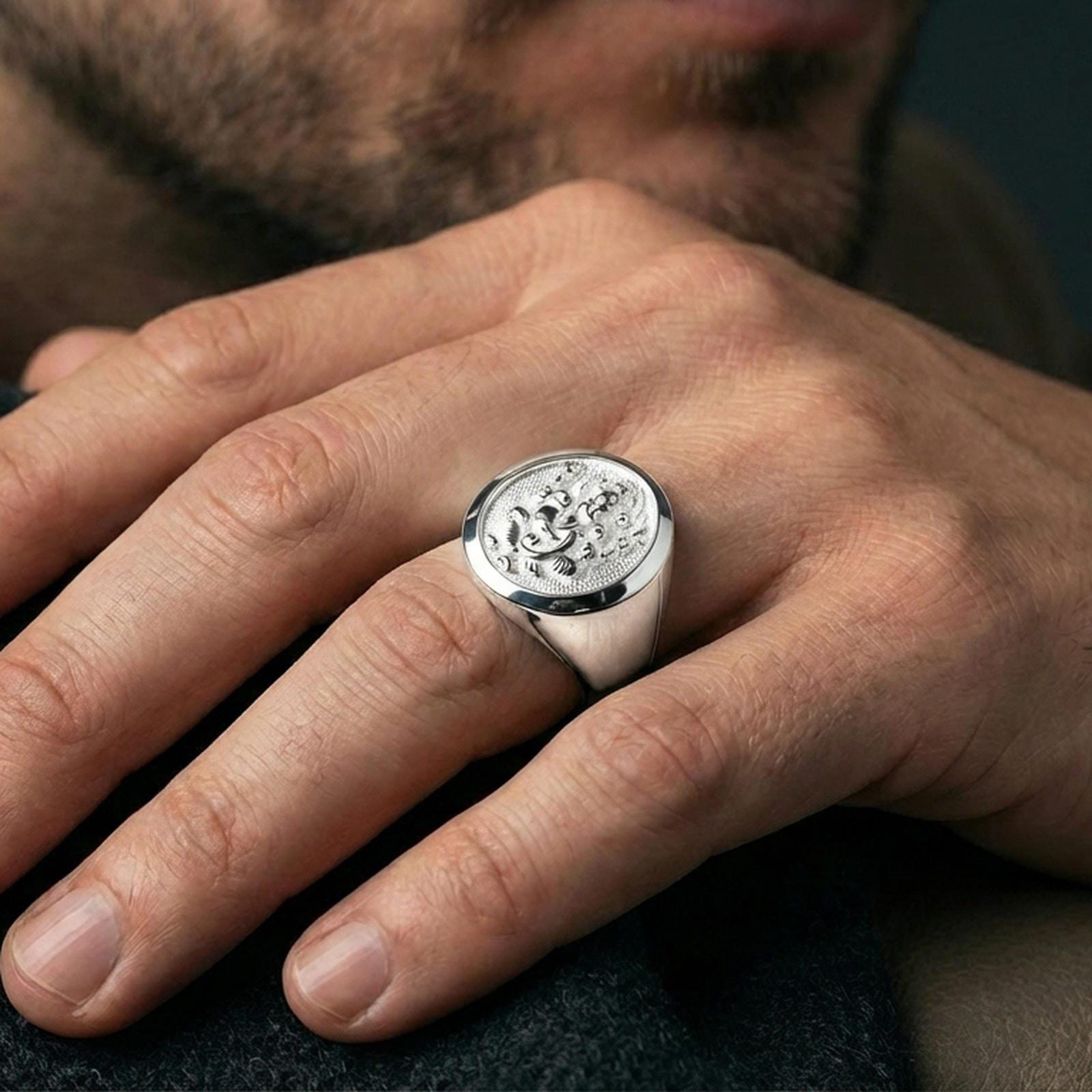 Polished silver Ganesha signet ring worn on finger, round signet face with engraved elephant god and smooth band