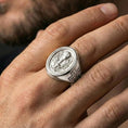 Load image into Gallery viewer, Polished silver Eucharist signet ring worn on finger, oval Christian signet ring with chalice, host, and ornate botanical motif
