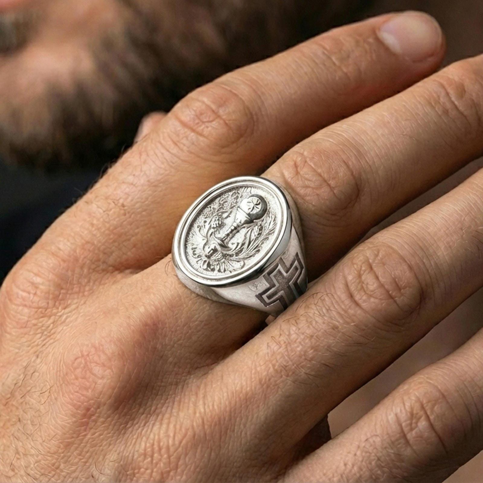 Polished silver Eucharist signet ring worn on finger, oval Christian signet ring with chalice, host, and ornate botanical motif
