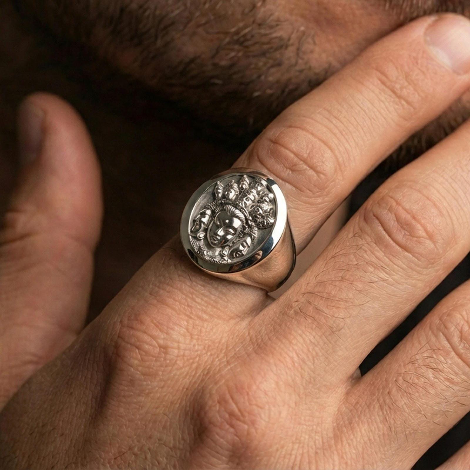 Polished silver spiritual signet ring worn on finger, oval multi-face deity engraving with clean reflective surface