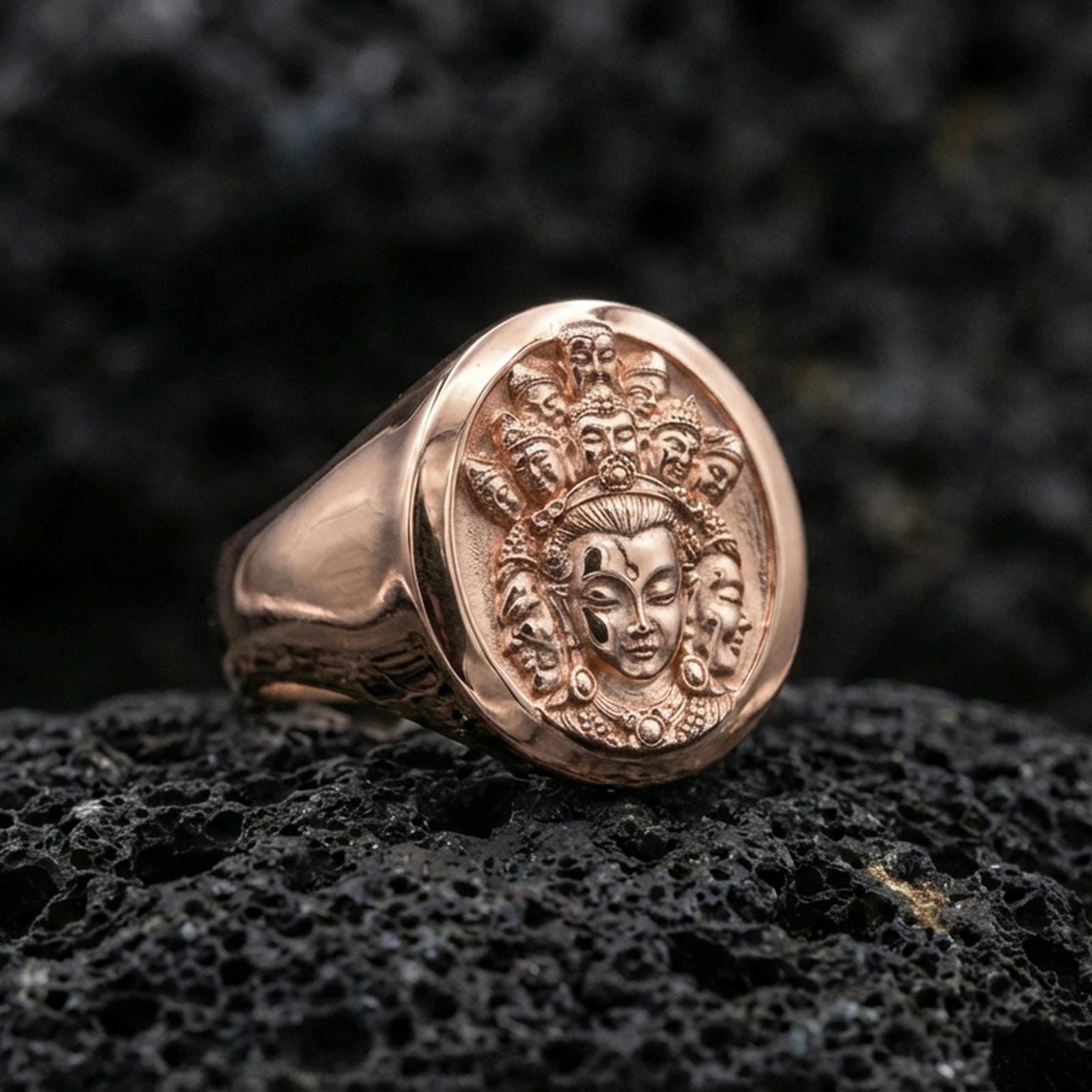Rose gold plated spiritual signet ring on volcanic stone, oval signet face with multi-faced deity relief and sculpted border