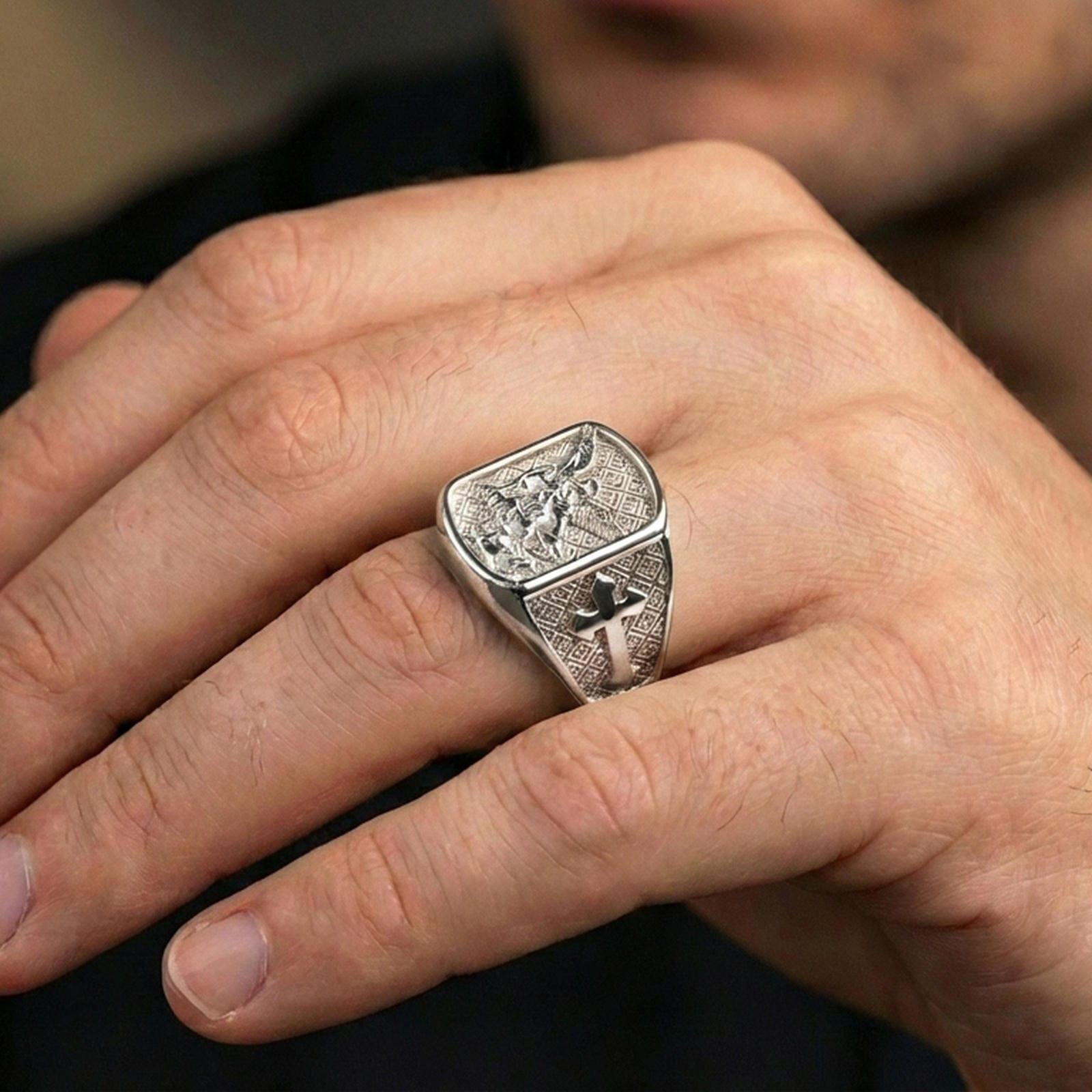 Polished silver Archangel Michael signet ring worn on finger, sculpted angel battle relief with bright reflective edges