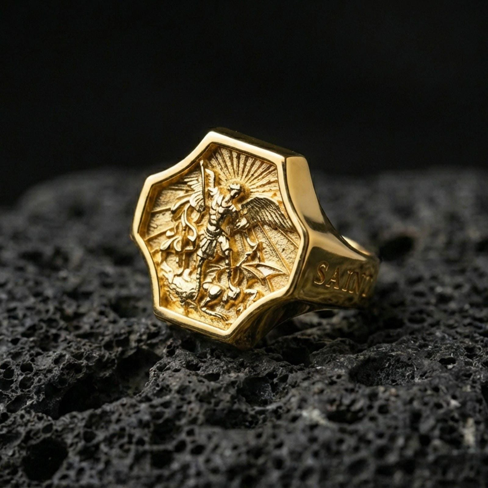 Gold plated Saint Michael ring on dark volcanic rock, Archangel warrior slaying dragon with engraved “SAINT” side text