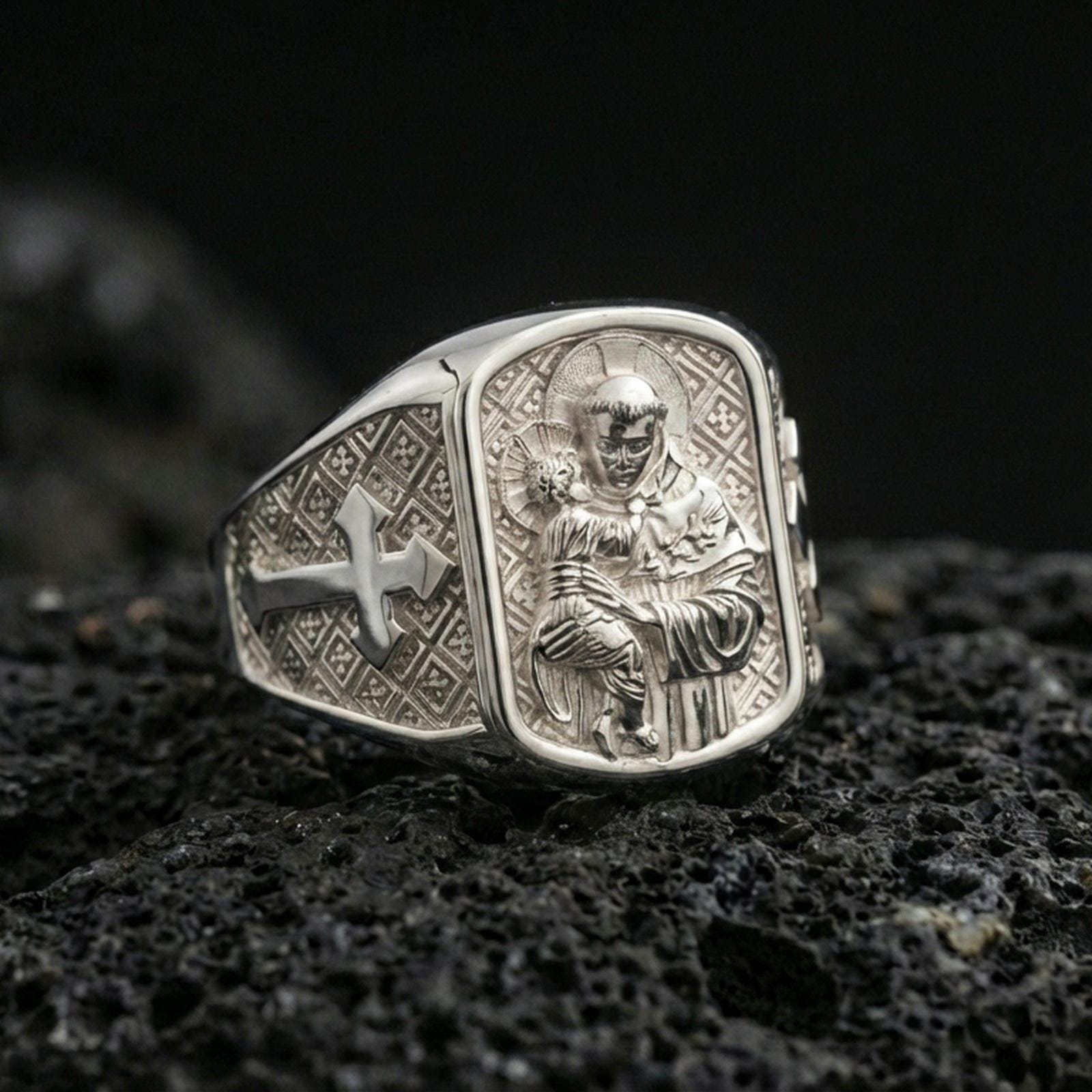 Polished silver Saint Anthony signet ring on porous volcanic stone, detailed saint and Child Jesus engraving with cross motif side