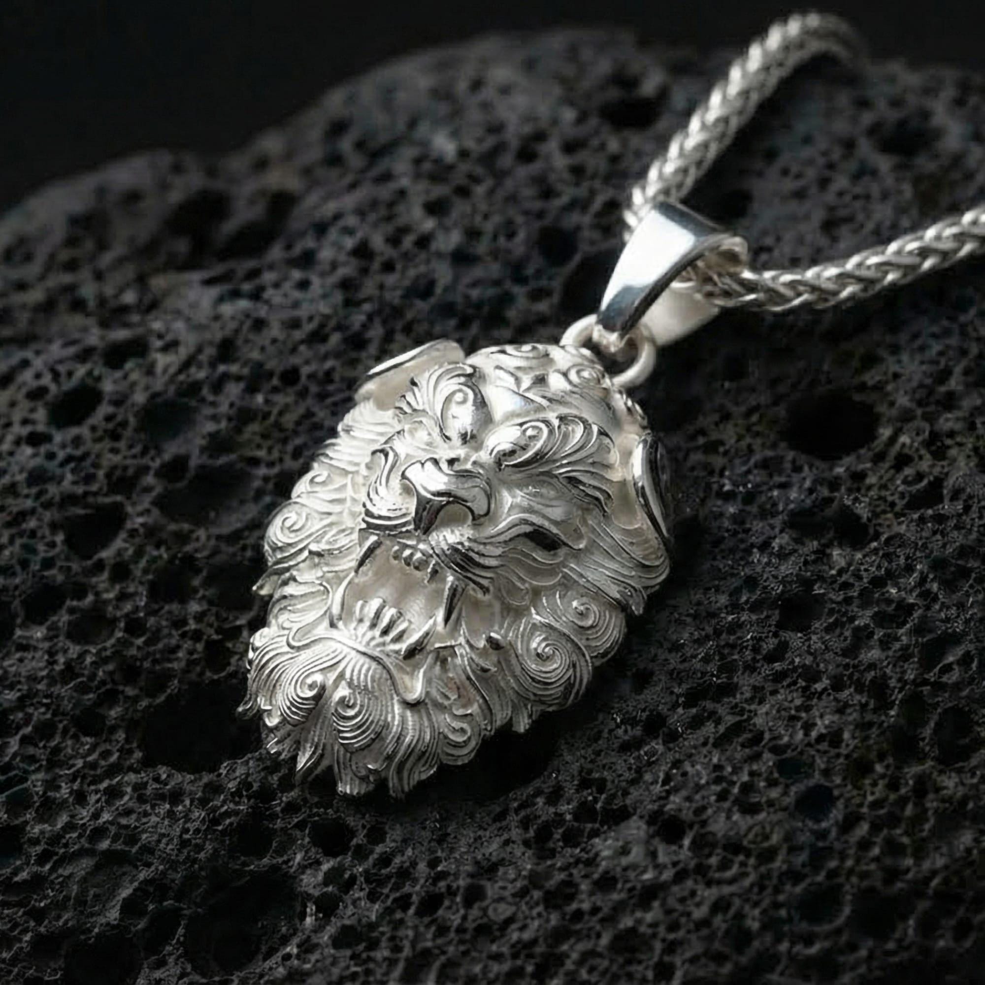 Polished silver Chinese guardian lion Fu Dog pendant displayed on volcanic stone background with sharp carved texture