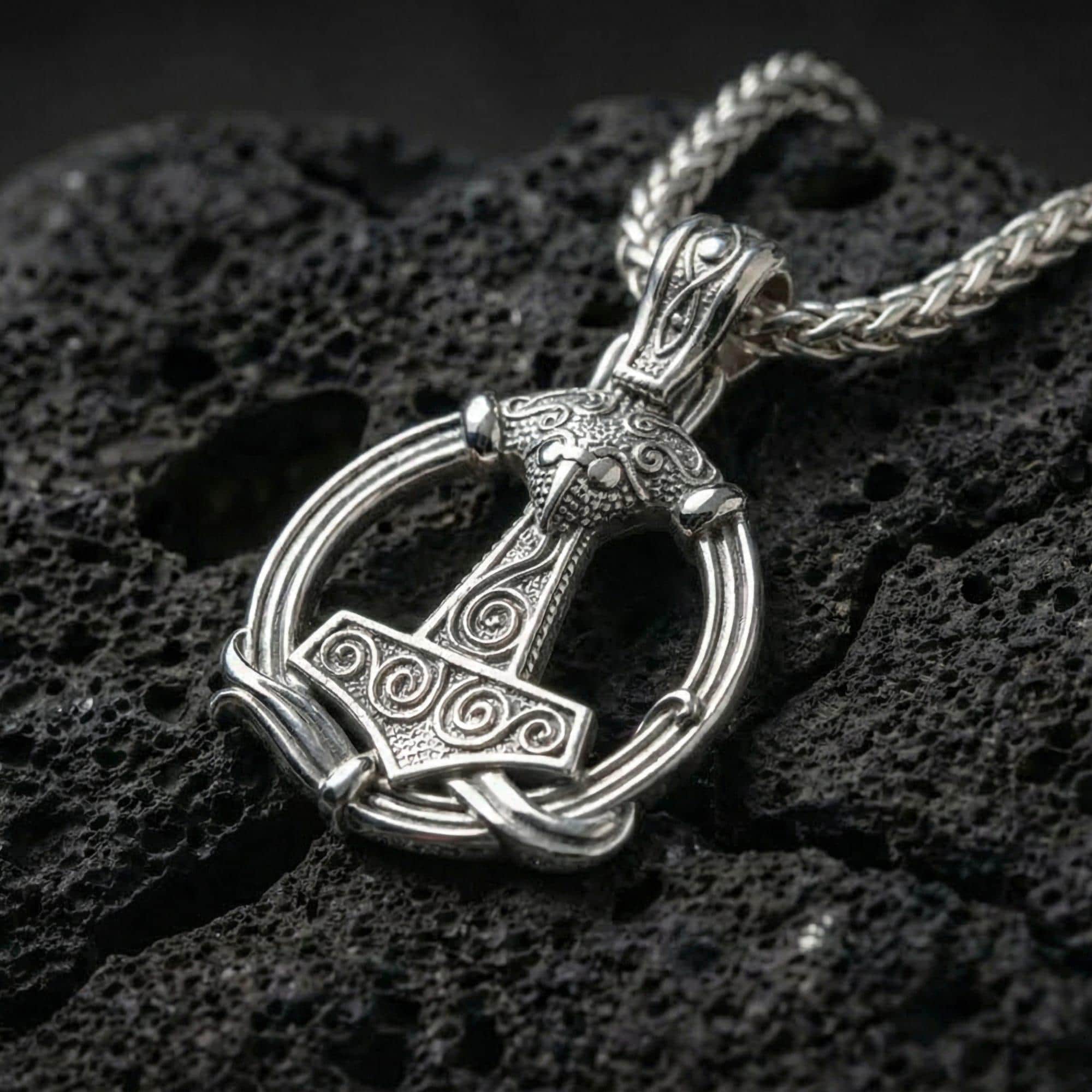 Polished silver Viking Mjölnir pendant necklace displayed on volcanic stone background with bold hammered texture