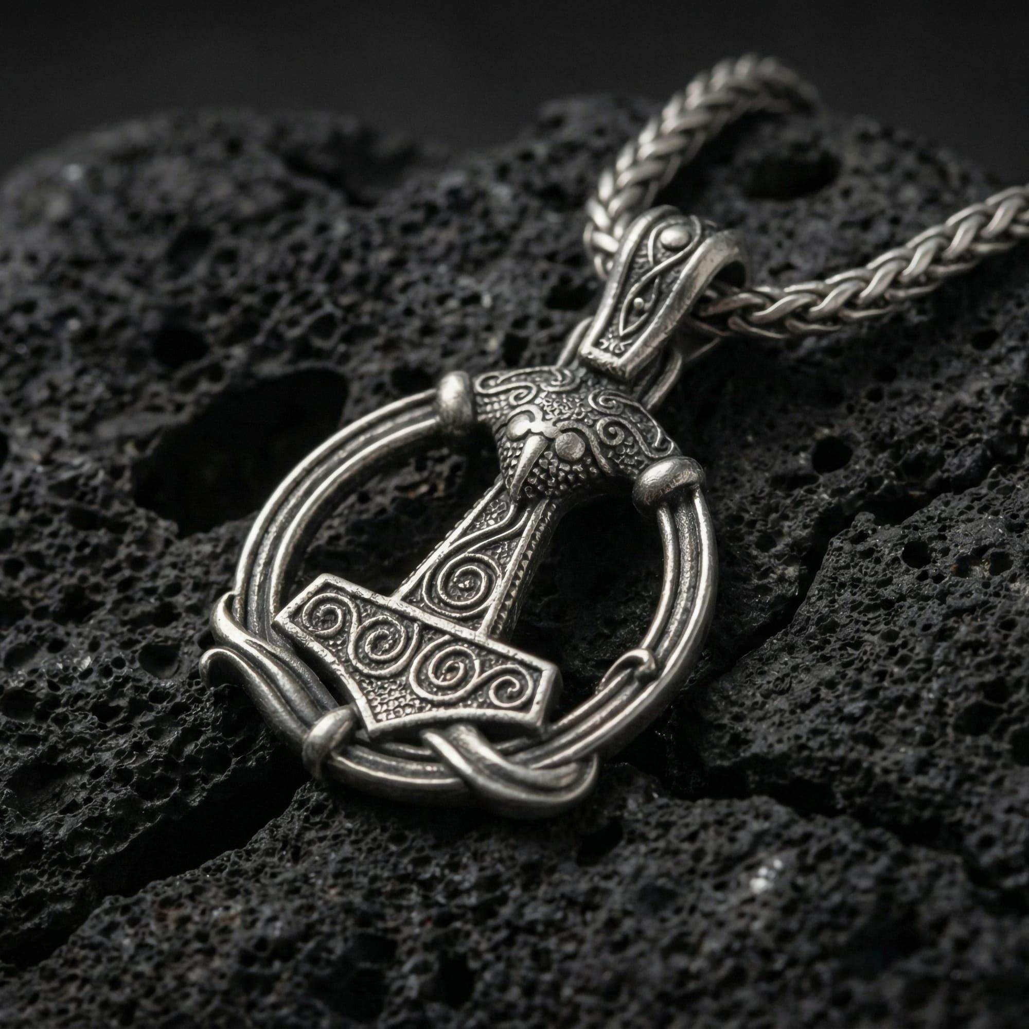Oxidized Thor’s Hammer Mjölnir pendant necklace photographed on volcanic rock with detailed Norse rune engraving