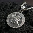Load image into Gallery viewer, Polished silver winged lion pendant necklace photographed on volcanic rock with detailed mythical griffin style relief and Greek key border
