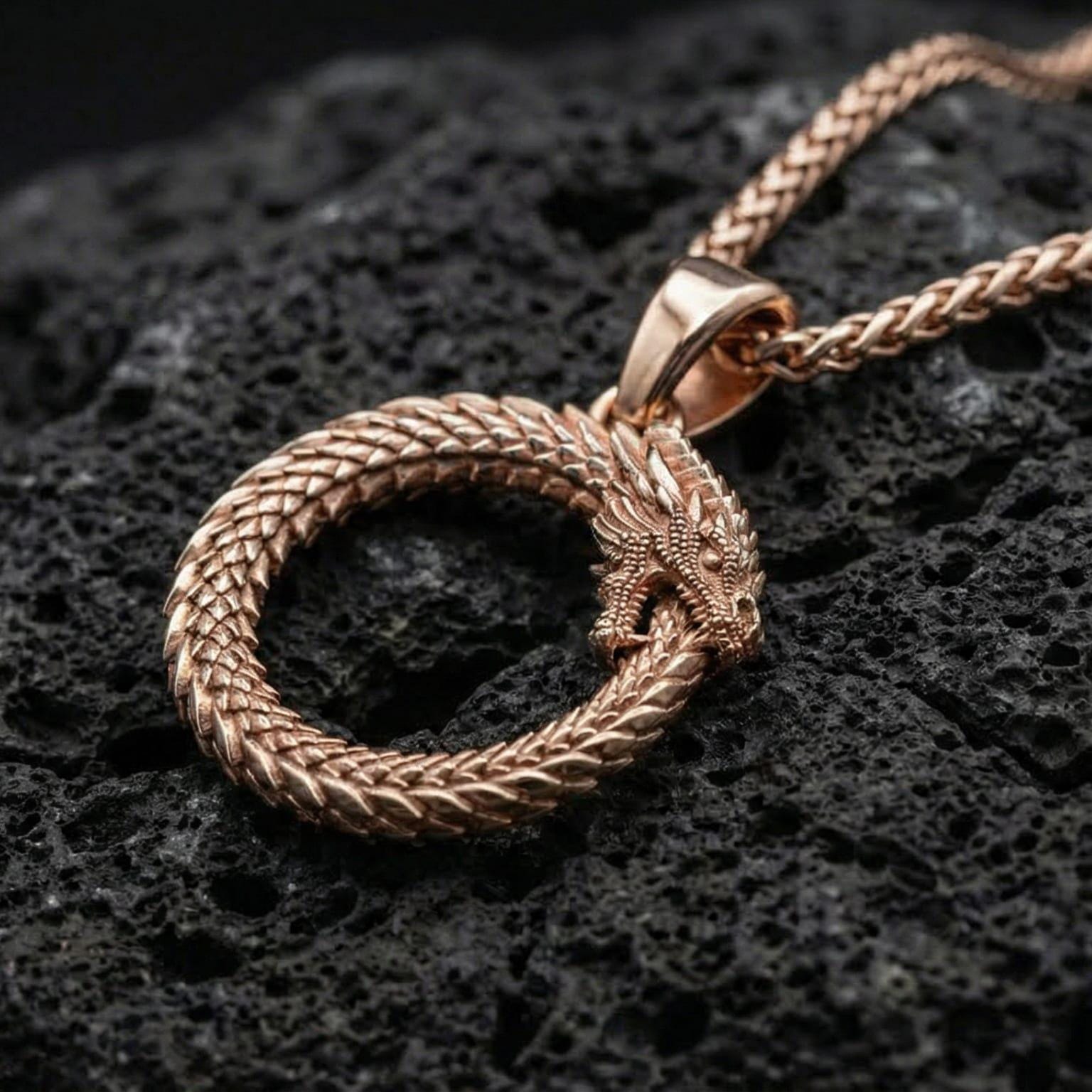 Rose gold plated ancient ouroboros snake pendant necklace presented on volcanic rock surface with mystical alchemical aesthetic