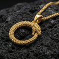 Load image into Gallery viewer, Gold plated ouroboros serpent pendant showcased on volcanic rock as a symbol of eternal cycle and renewal
