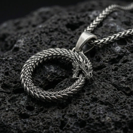 Oxidized ouroboros serpent pendant necklace photographed on volcanic rock with detailed ancient mythology scale texture