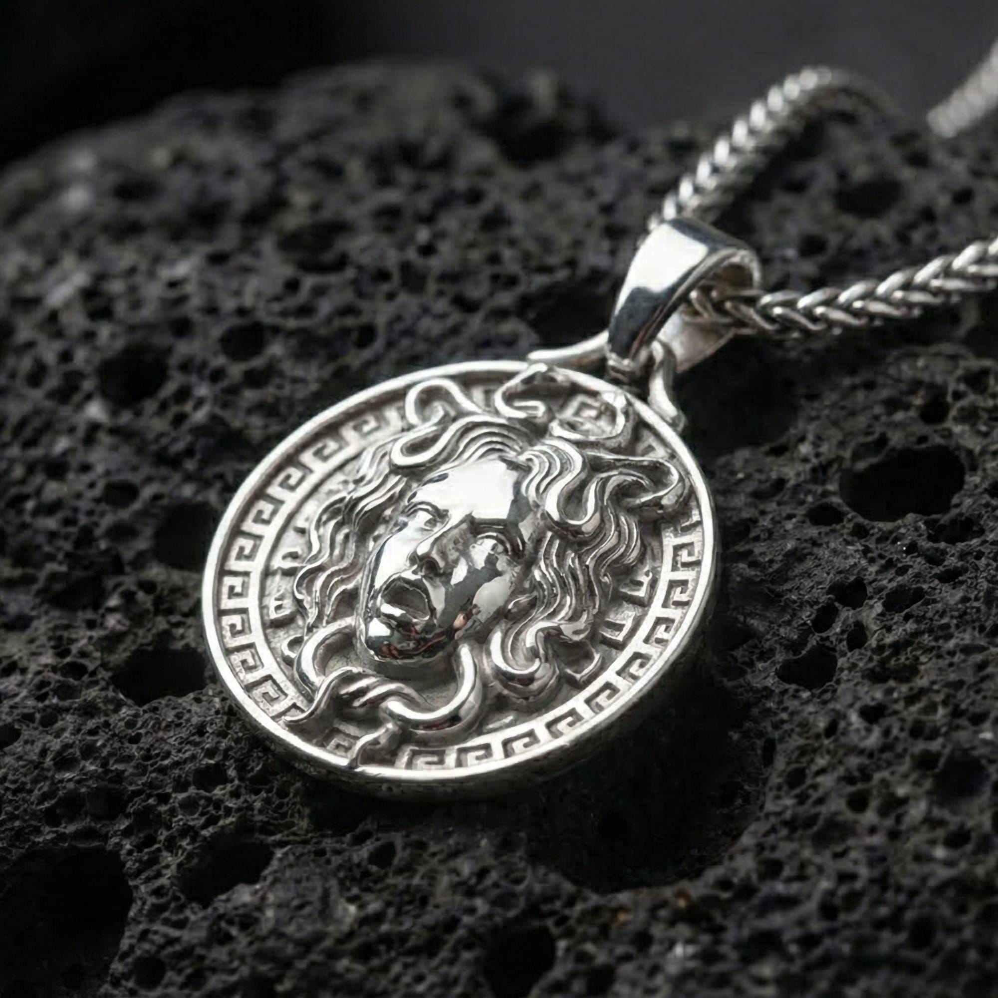 Polished silver Medusa Greek mythology pendant displayed on volcanic stone background with sharp sculpted facial detail