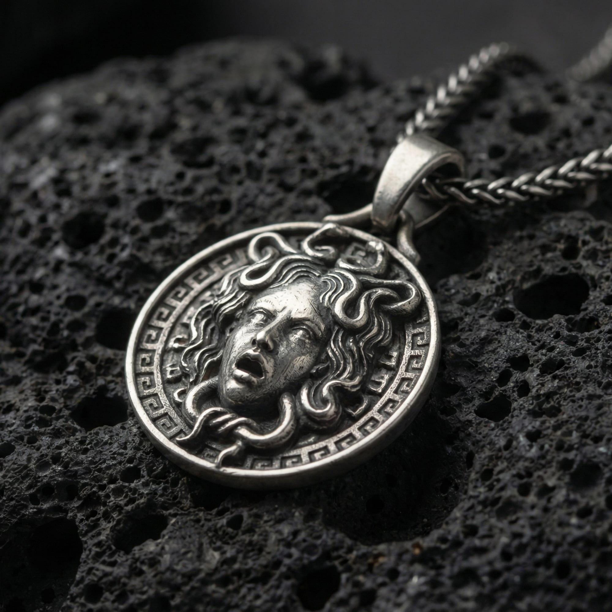 Oxidized Medusa necklace pendant photographed on volcanic rock with detailed snake hair relief and Greek key border