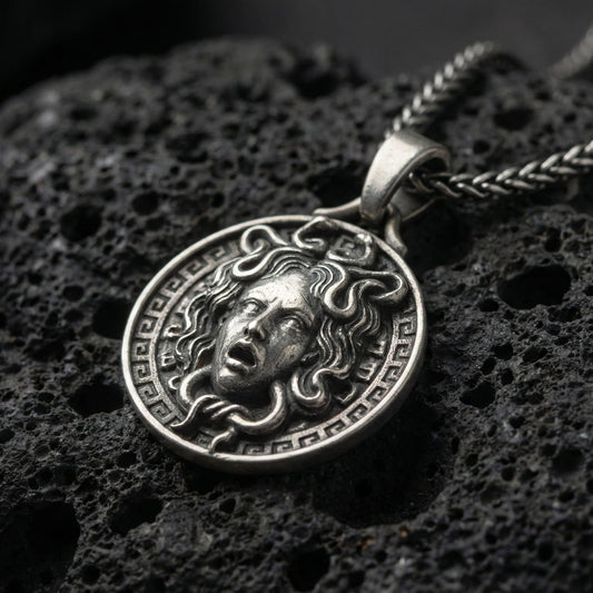 Oxidized Medusa necklace pendant photographed on volcanic rock with detailed snake hair relief and Greek key border